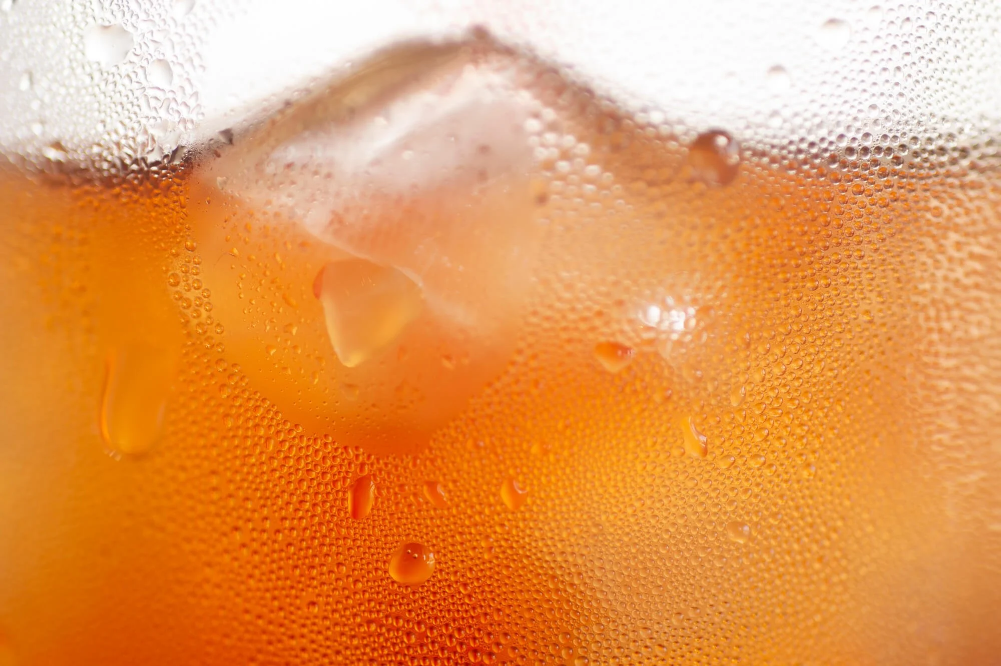 Close-up of a glass of cola with ice cubes, showing condensation and bubbles on the surface.