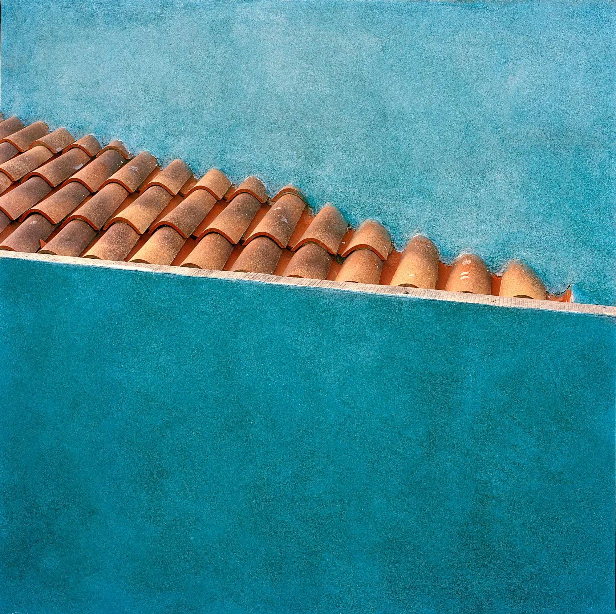 Close-up of a blue stucco wall with terracotta roof tiles underneath.