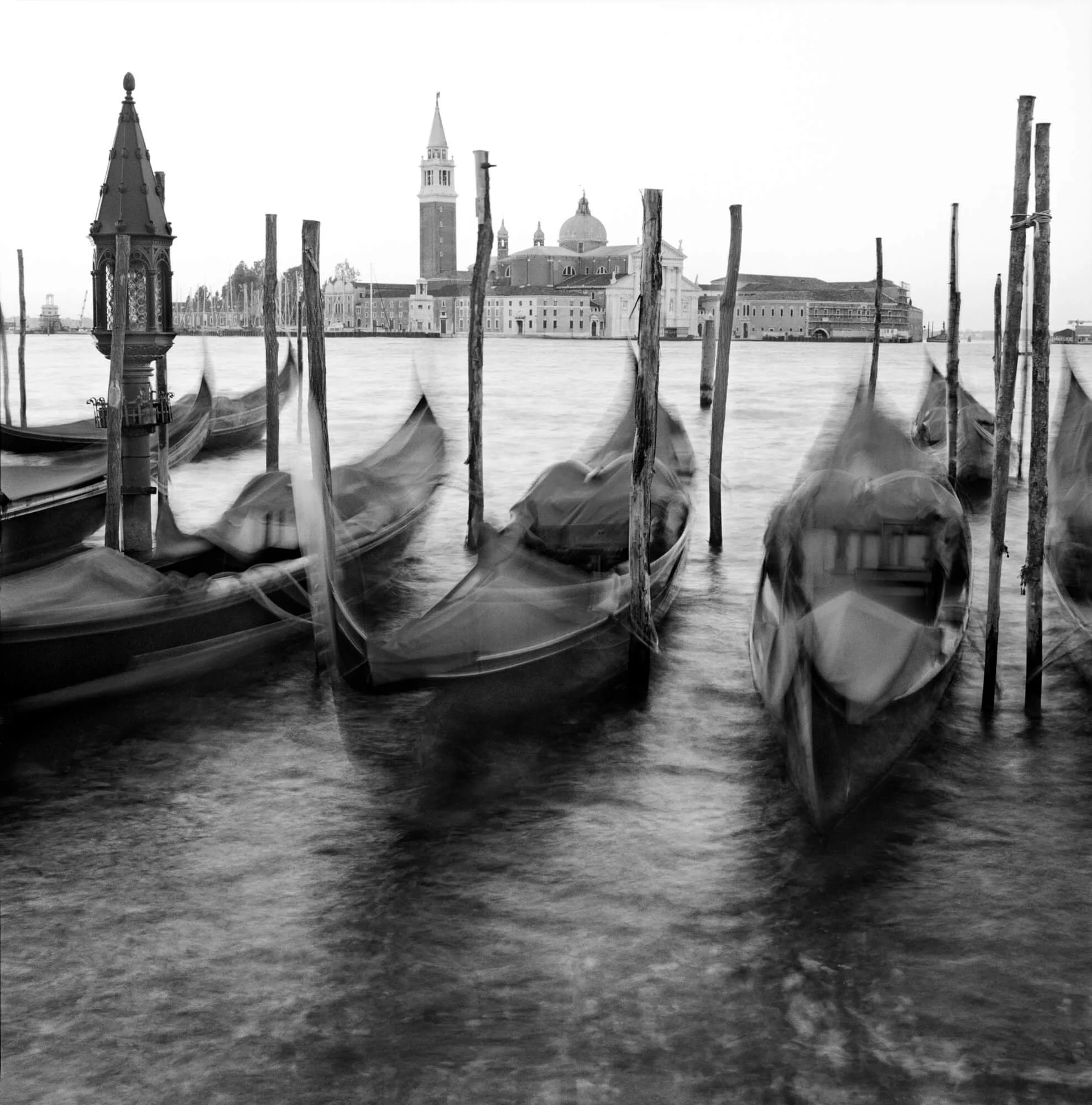 Black and white photo of gondolas docked in Venice with the Basilica di San Marco in the background.