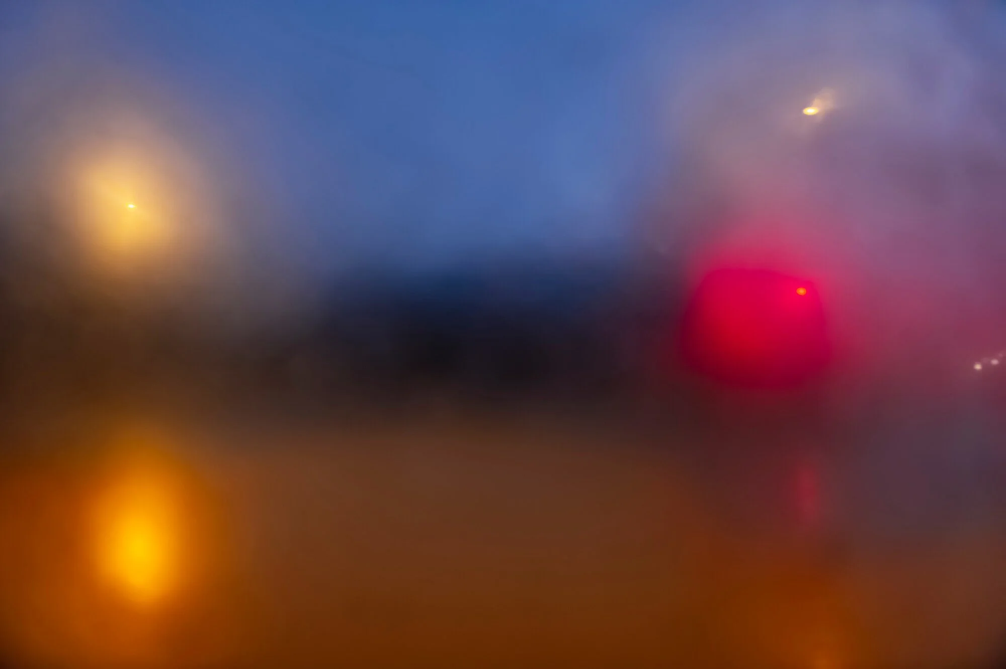 Blurred view of city lights through a rain-covered window at night.