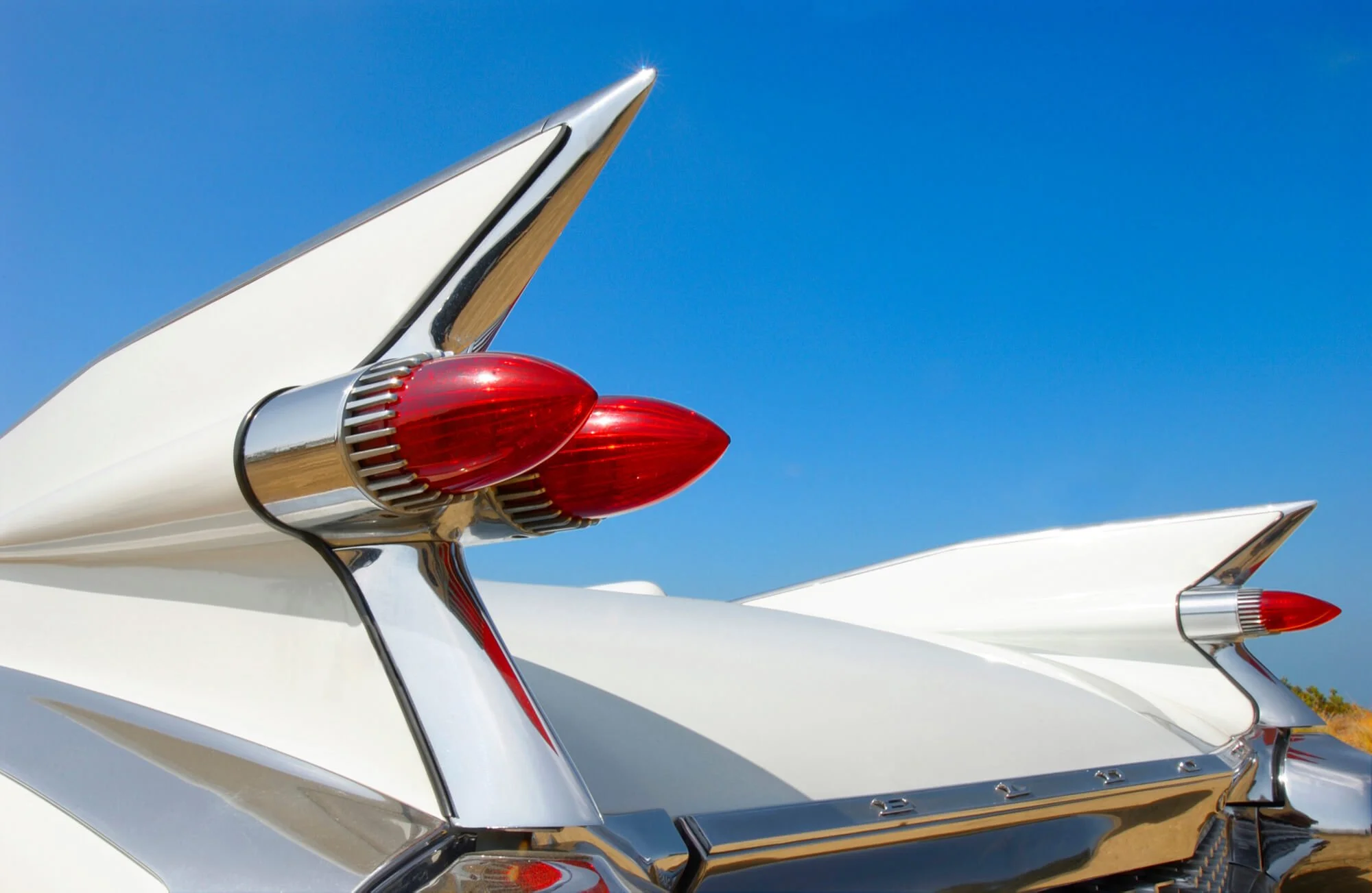 Close-up of the tail fins and red rocket-shaped taillights of a classic white vintage car against a blue sky.