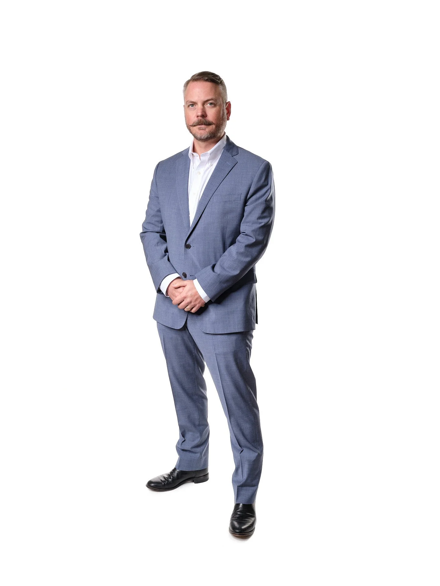 A man in a light blue suit with a white shirt standing against a white background.