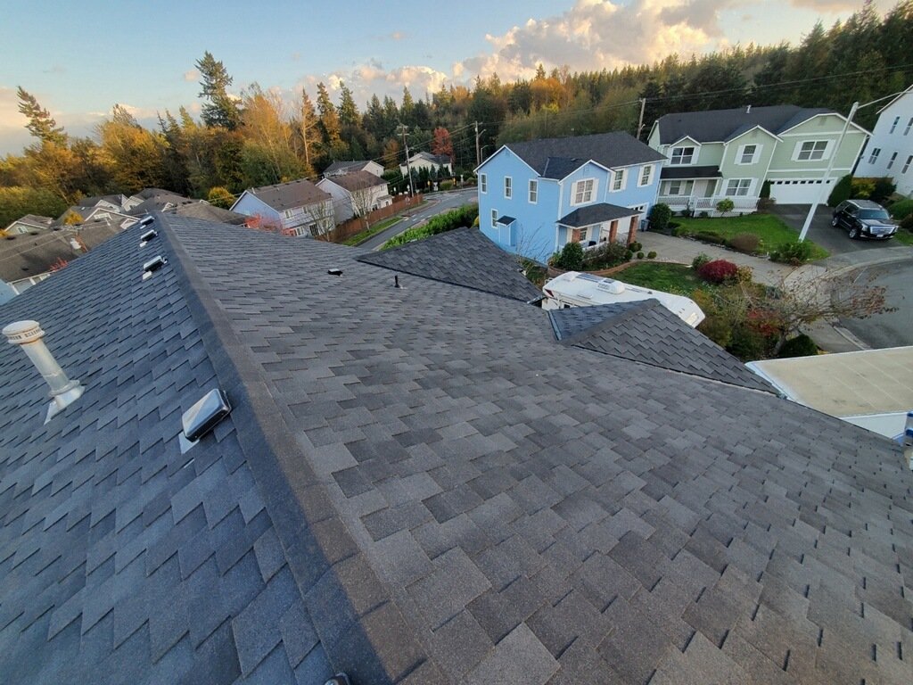 Aerial view of rooftops in a suburban neighborhood with various colored houses, trees, and a partly cloudy sky in the background.