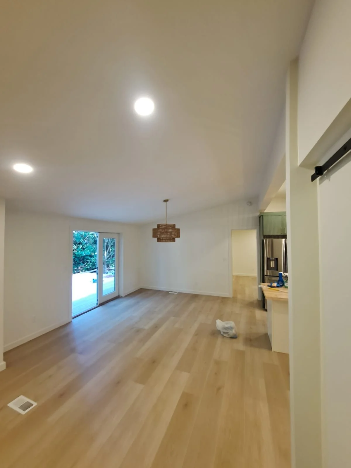 Empty living room with hardwood flooring, sliding glass door leading outside, modern chandelier, and white walls.