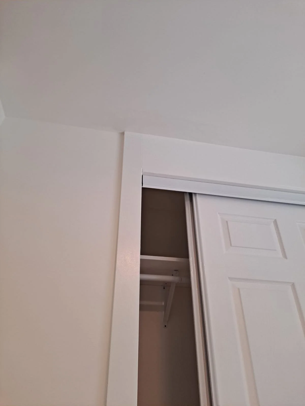 A closet with a sliding white door partially open, revealing a shelf and hanging rod inside.