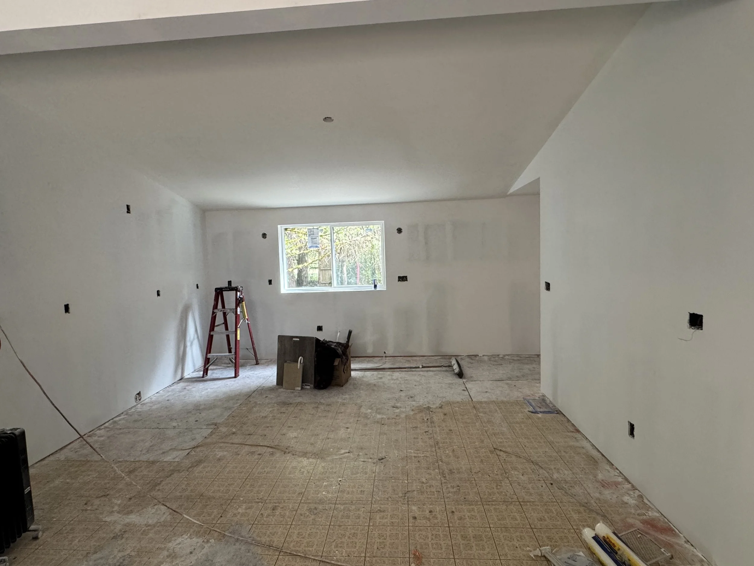 Interior room under renovation with drywall walls, construction tools, ladder, and unfinished flooring.