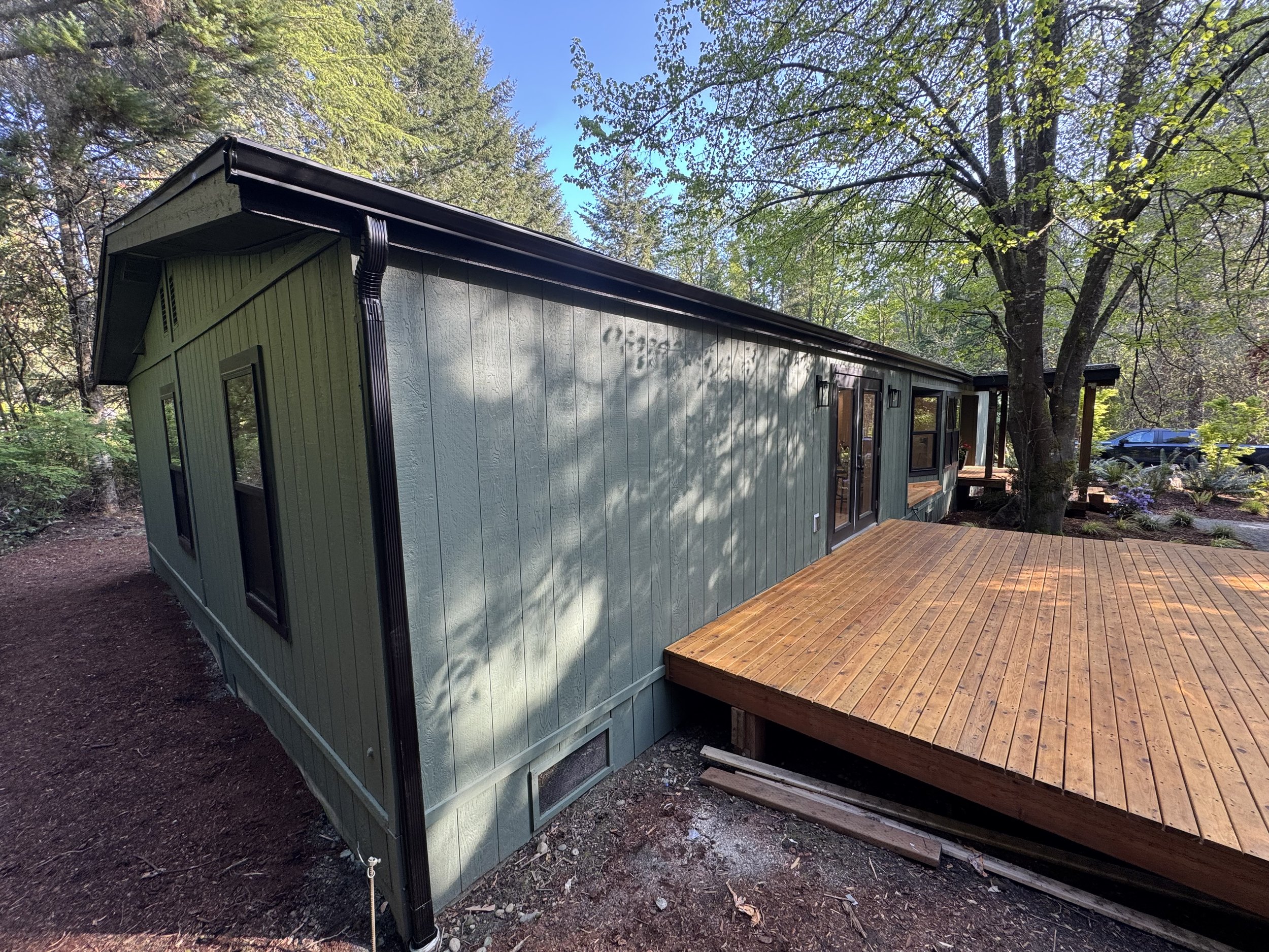 A green house with a wooden deck surrounded by trees and greenery.