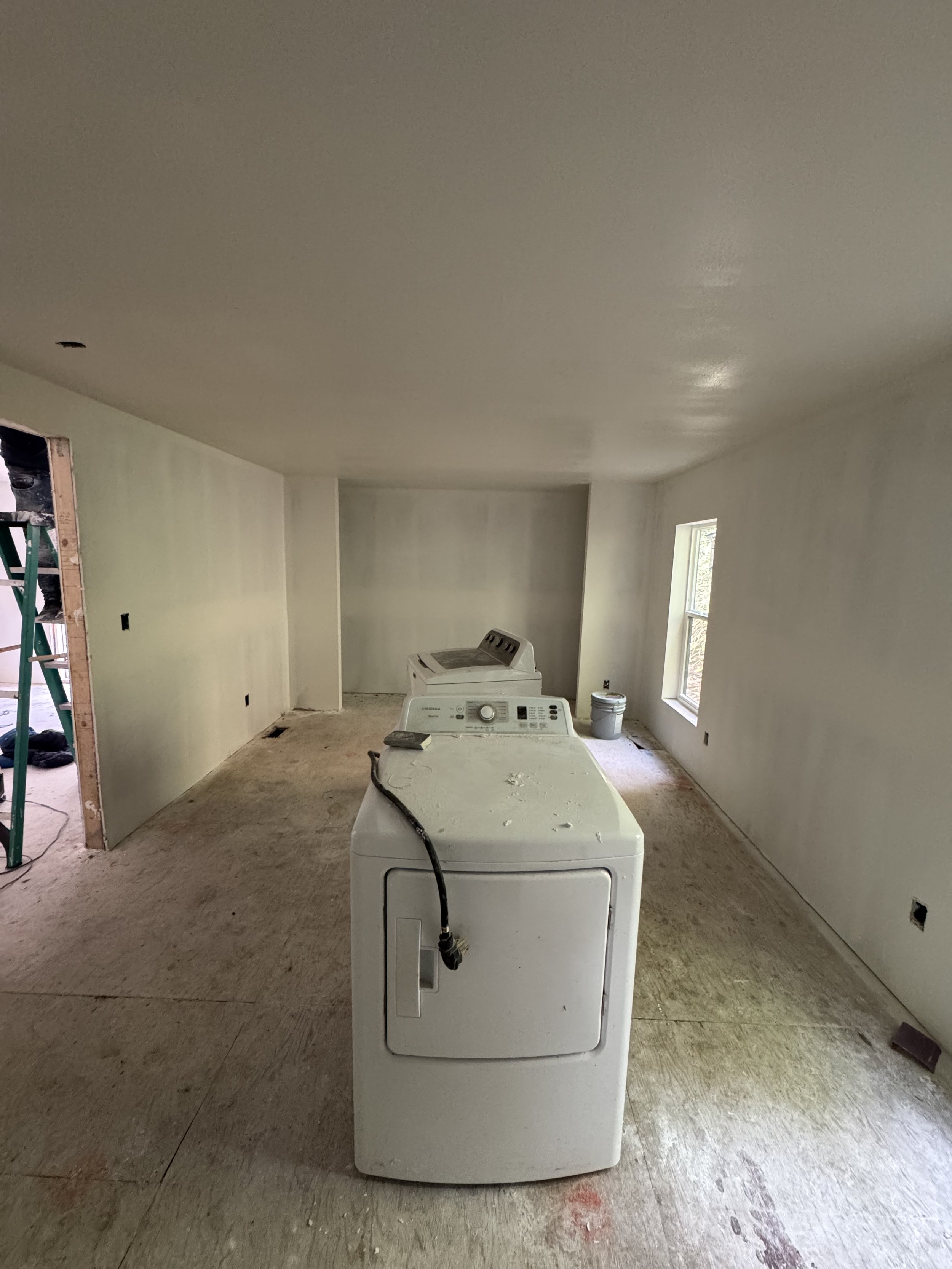 Laundry room under construction with a white washing machine and dryer, unfinished floor, and drywall walls.