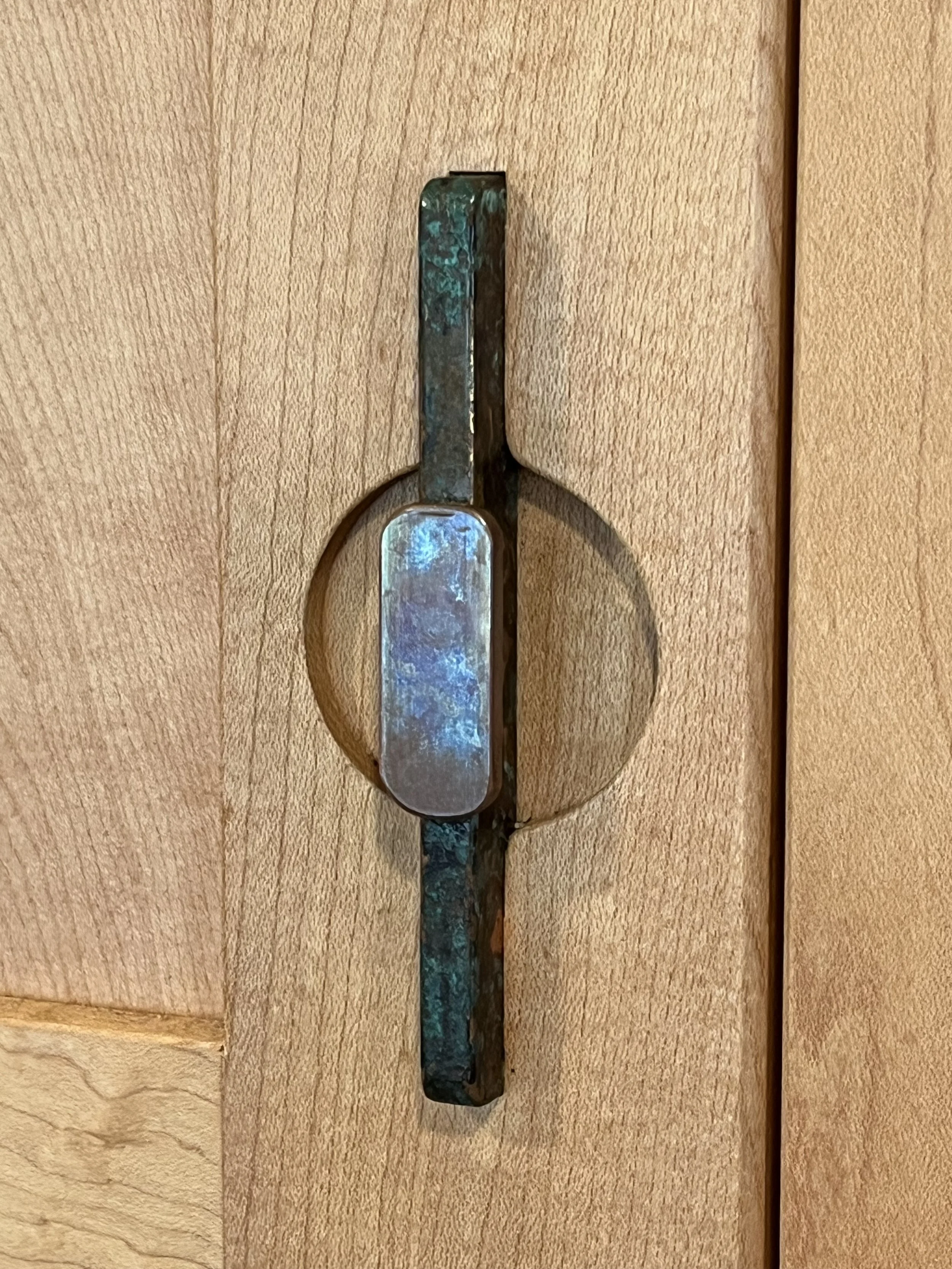A close-up view of a door latch with a metallic, aged, and slightly rusted appearance mounted on a wooden door.