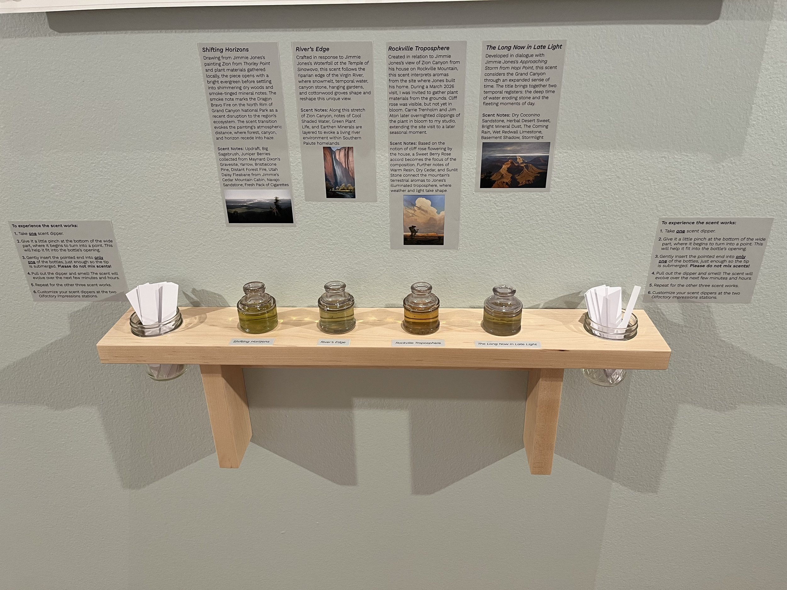 Display board with descriptions of four scent experiences, with small jars of scents and scent papers in front of it.