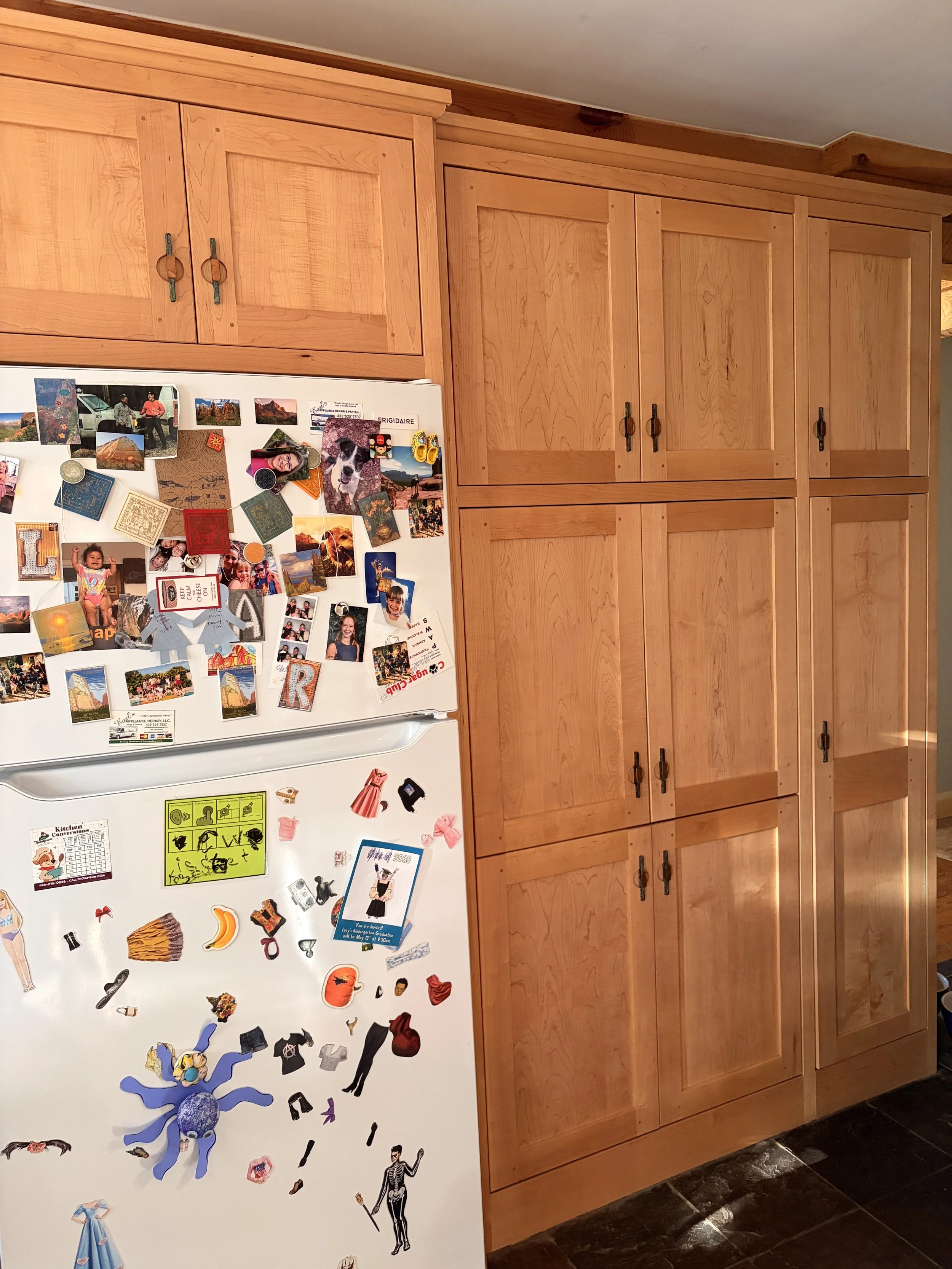 Kitchen with wooden cabinets and a white refrigerator covered with various magnets and photos.