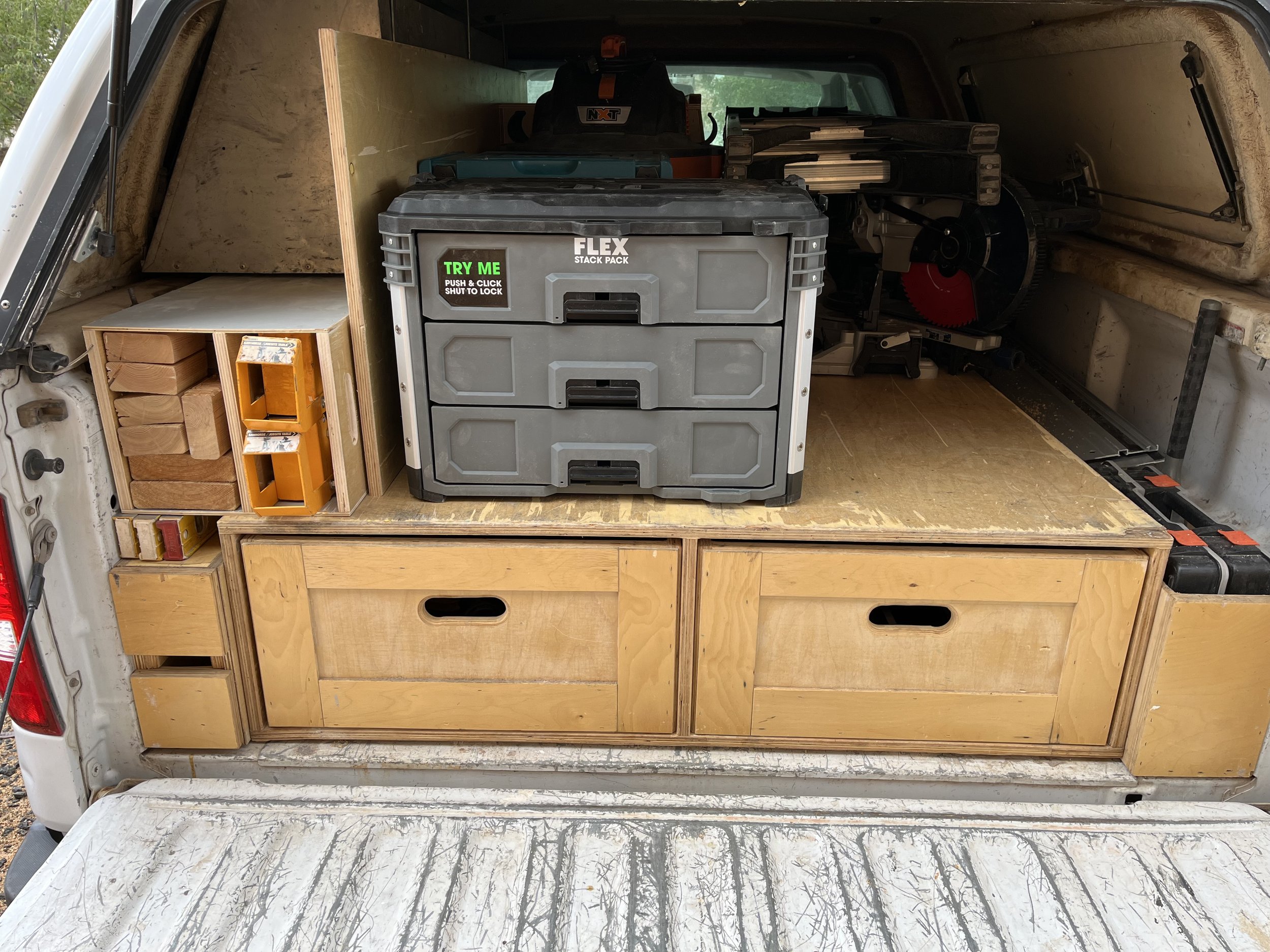 Back of a van converted into a storage space with wooden cabinets, a plastic tool chest, and power tools.