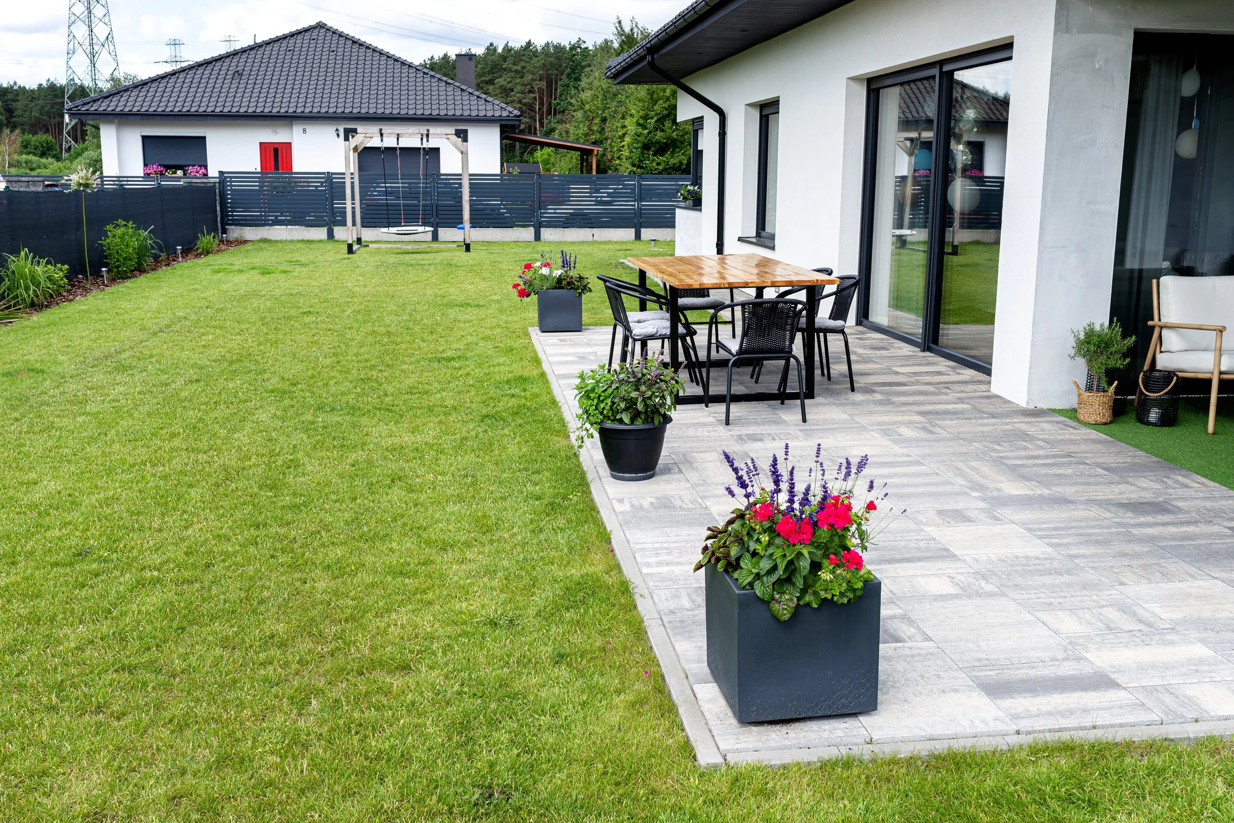 Backyard with patio, outdoor dining set, potted flowers, lawn, and a swing