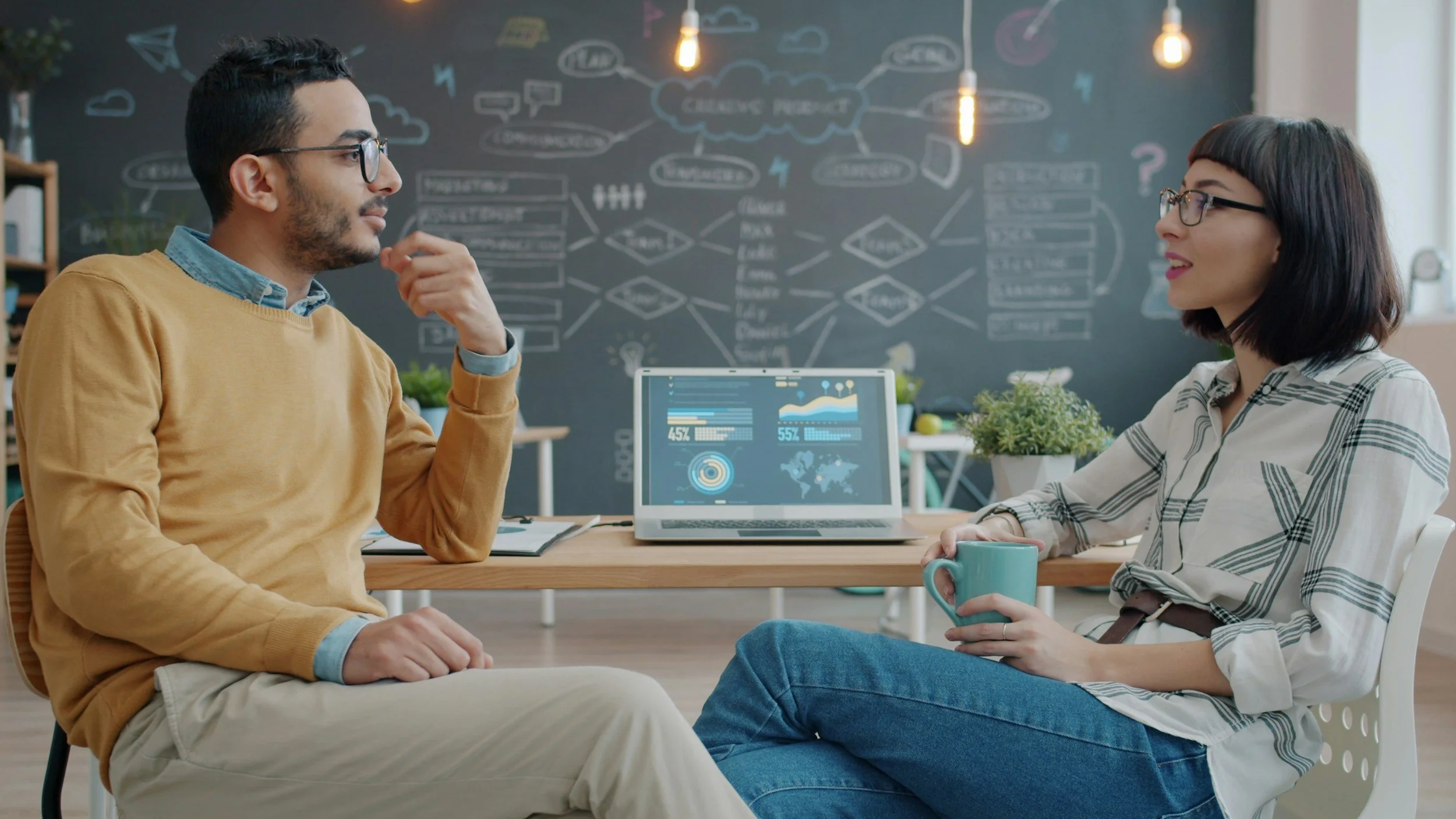 A man and a woman facing each other having a feedback conversation upfront on an open laptop