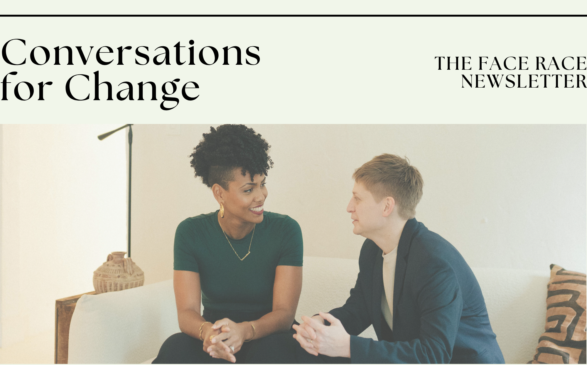 A woman and a transperson talking and smiling while sitting on a couch in a casual setting.