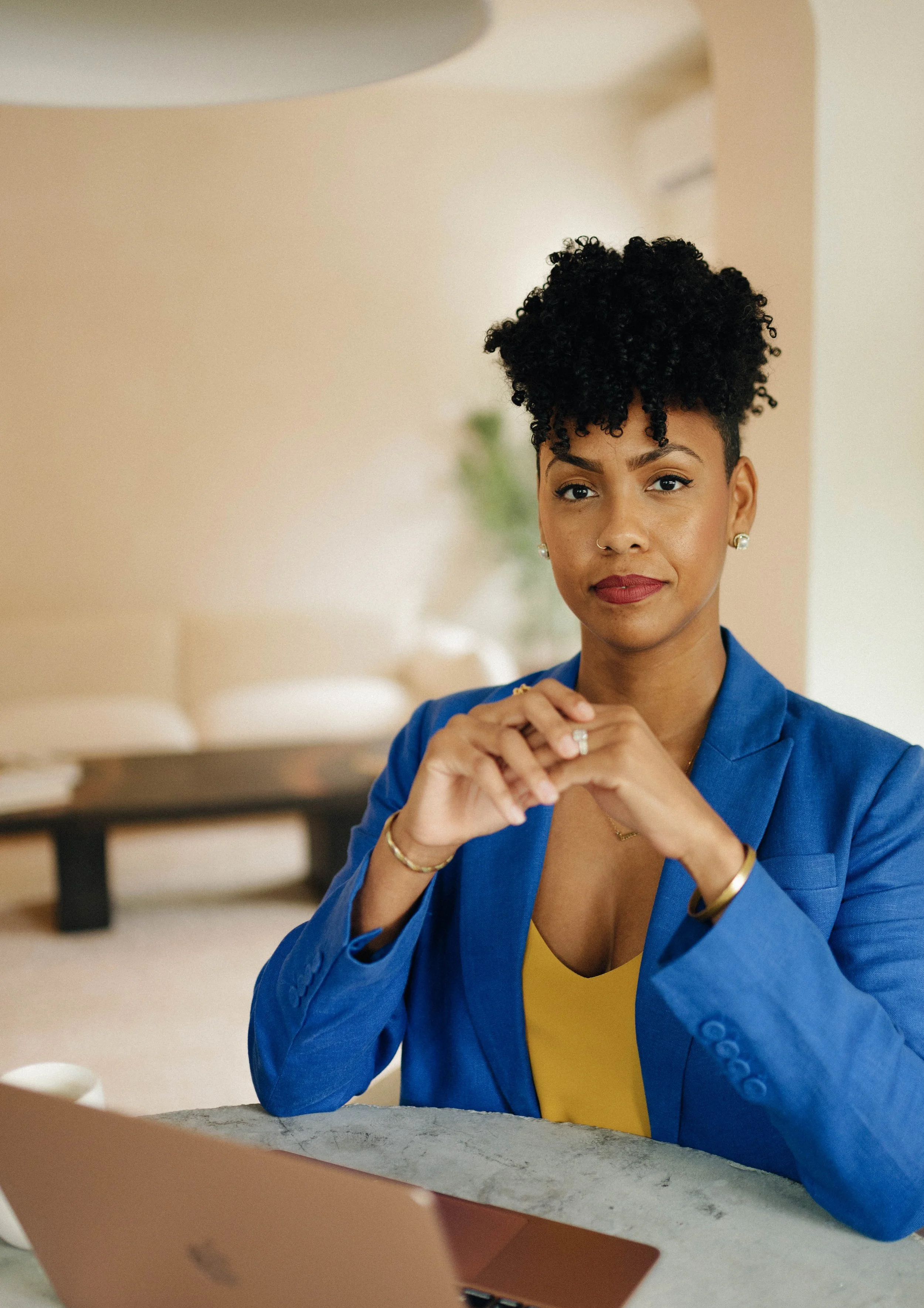Black woman in a blue suit sitting at a desk upfront of an open laptop