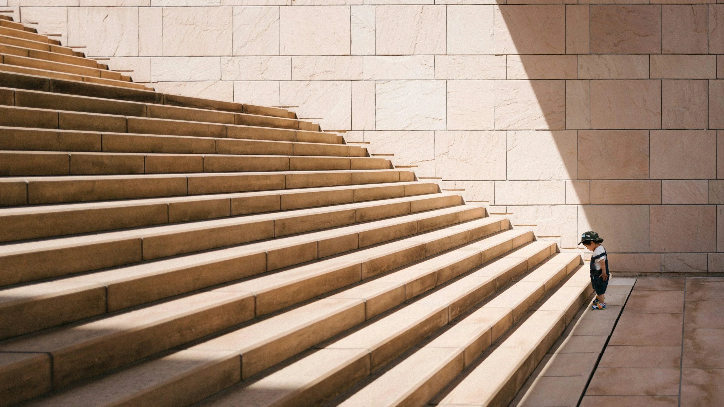 Small child at the foot of a large, sunlit staircase