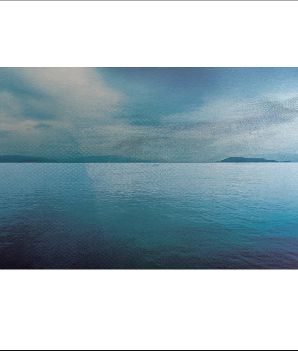 Wide view of a calm body of water under a cloudy sky, with distant landmasses on the horizon.