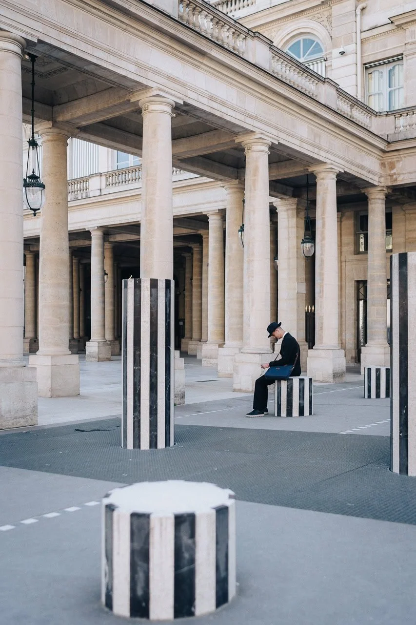 A lone well dressed man sat on the columns in Palais Royal, Paris