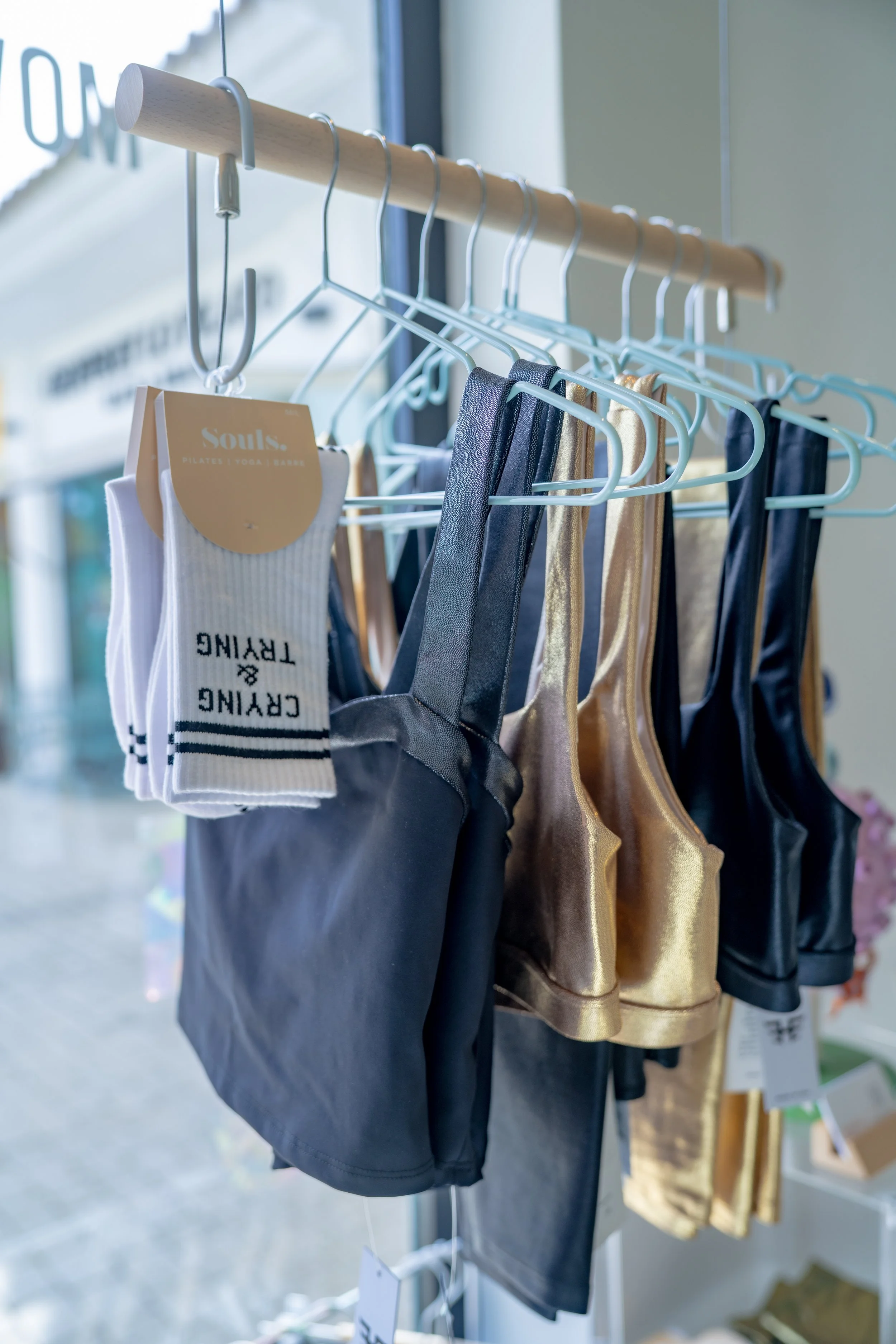 Clothing rack displaying Heroine Sports Active wear in black, gold, and dark gray bags along with a pair of white Souls grip socks with black lettering, inside a store near a window.