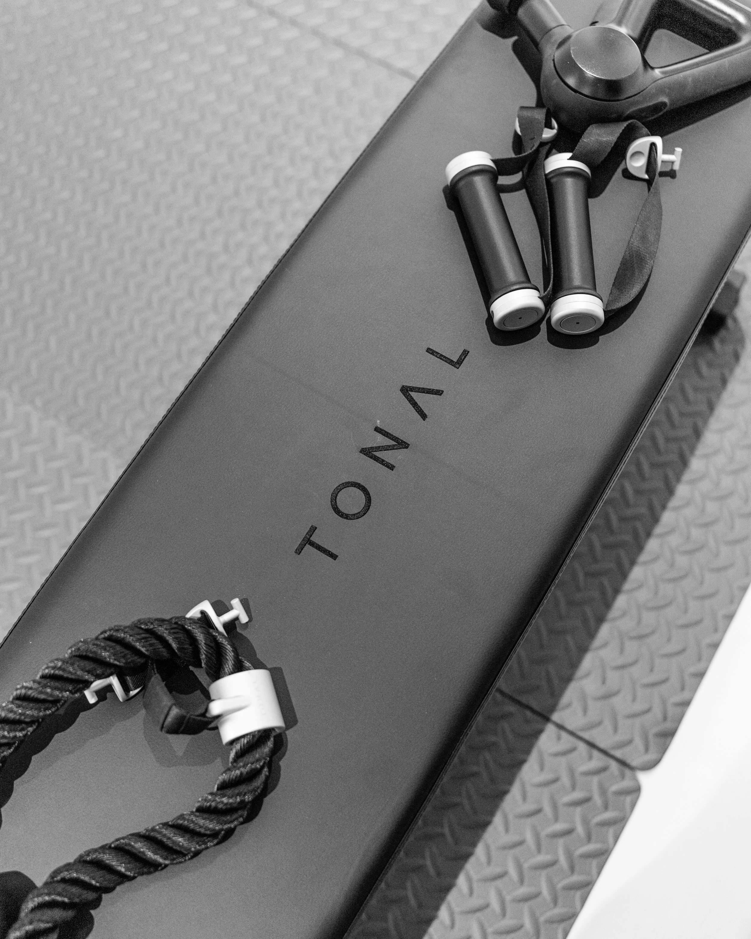 A black workout bench with the word 'TONAL' on it, a jump rope, and folded resistance bands on top.