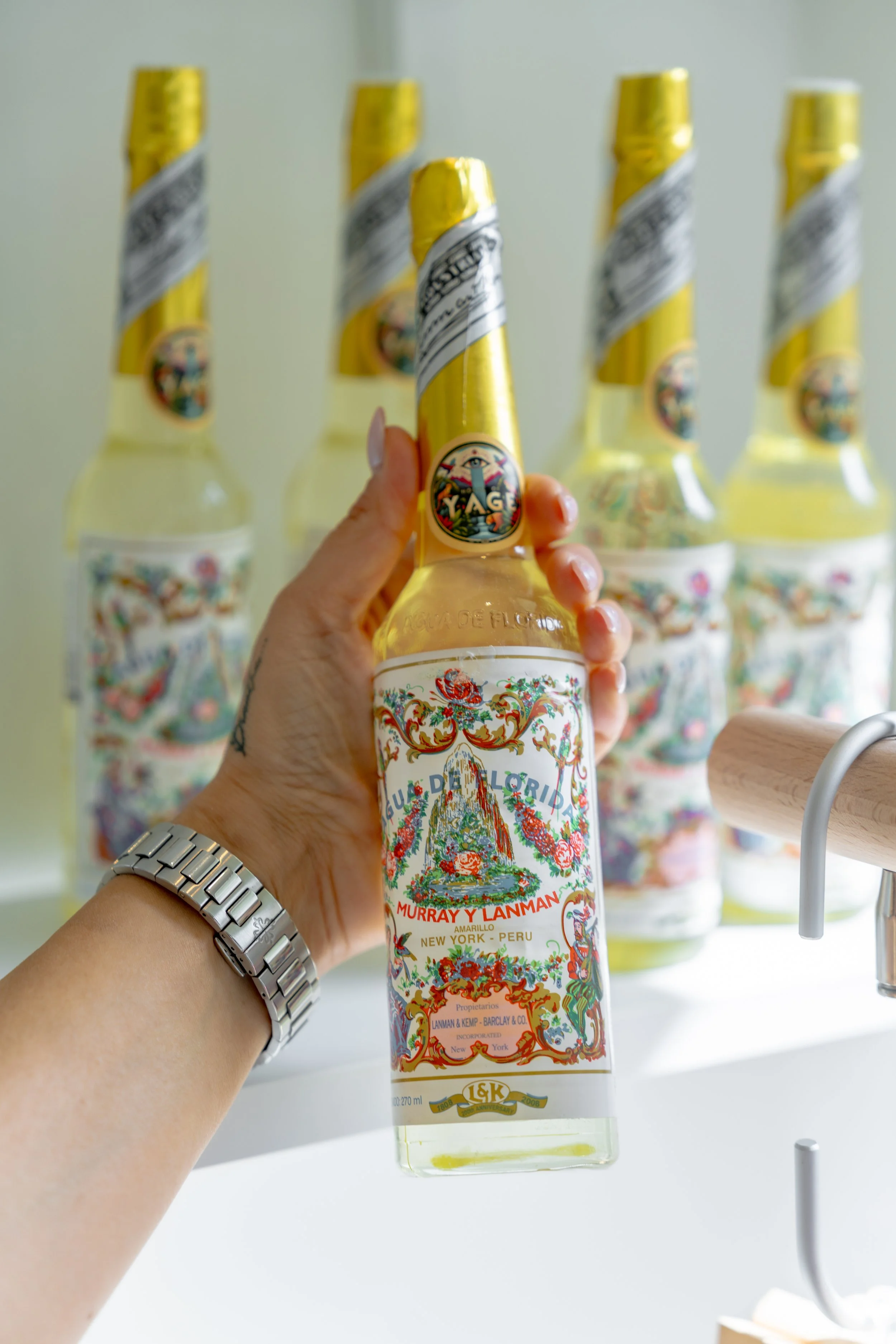 A hand holding a bottle of Yaguara liquor with four similar bottles blurred in the background.