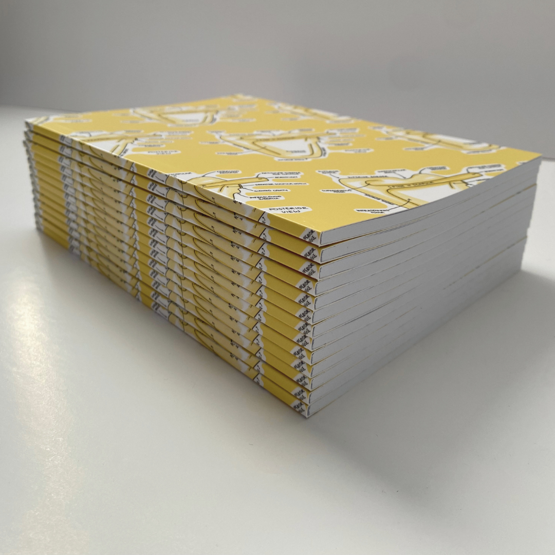 A stack of A5 anatomy-notebooks shown together in a pile, with a scapula pattern repeated on a yellow background