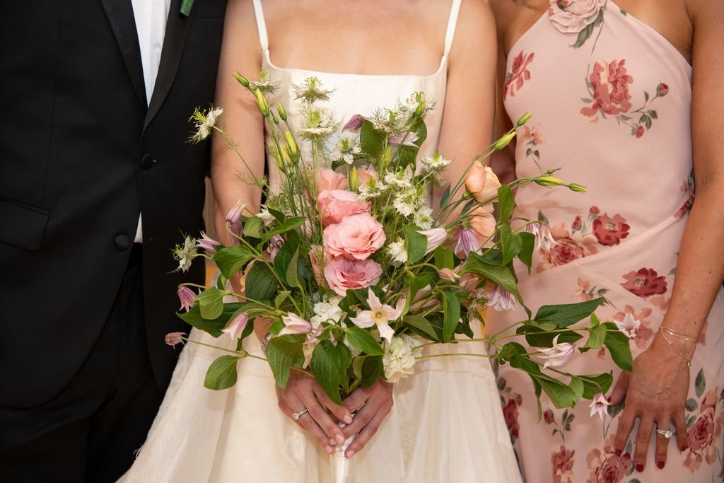 Woman in a white wedding dress holding a bouquet of flowers, smiling outdoors