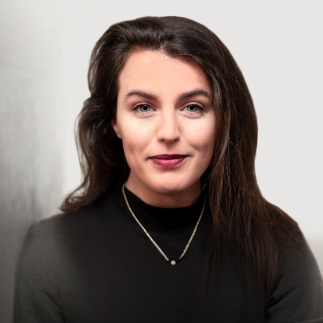 Woman with long brown hair wearing a black turtleneck and necklace, smiling at the camera.
