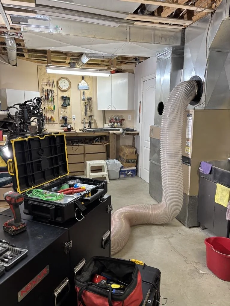 A garage workshop with tools hanging on a pegboard, a clock, a workbench, and a flexible duct air intake connected to a vent system.