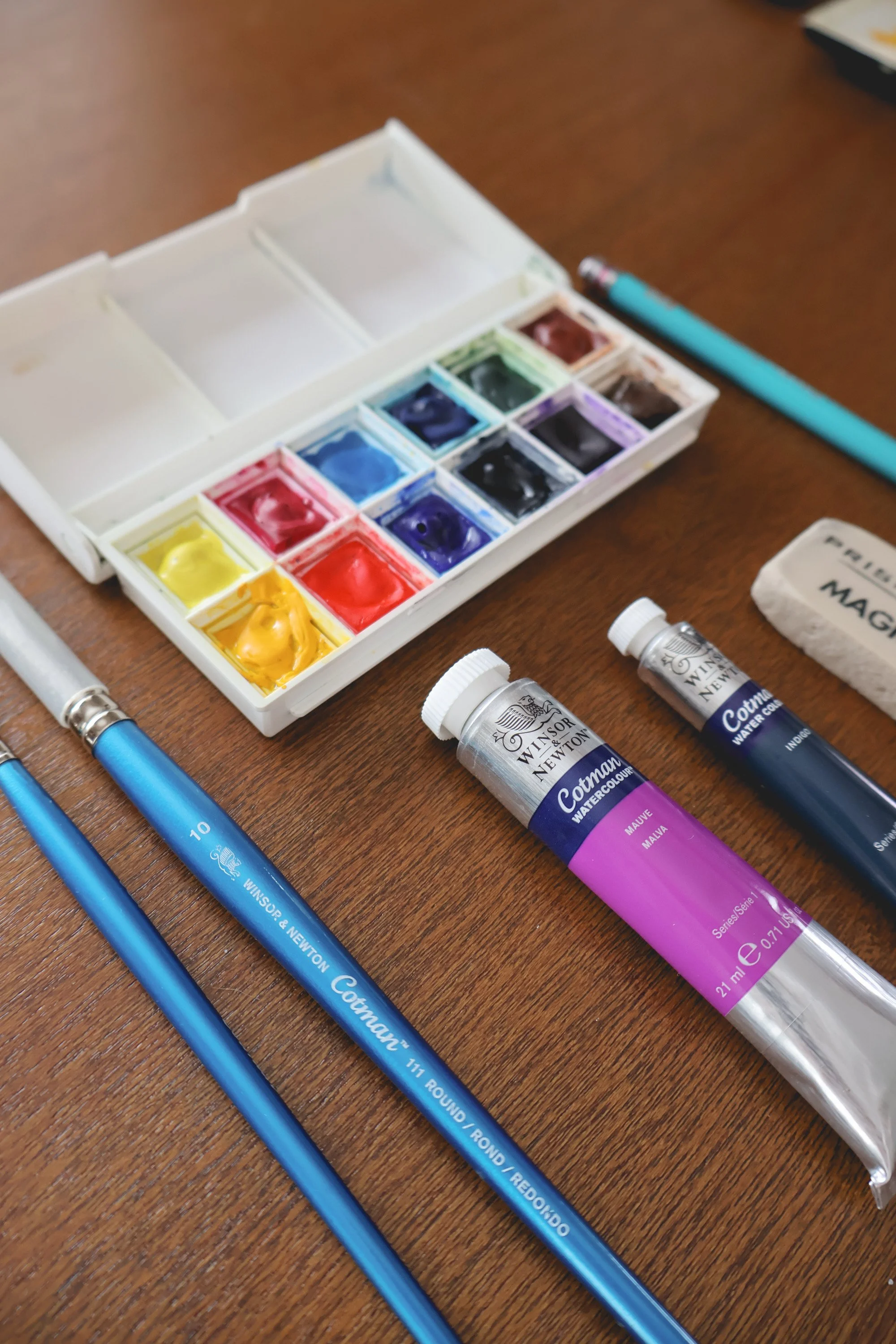 watercolor palette full of paint surrounded by paintbrushes and tubes of paint