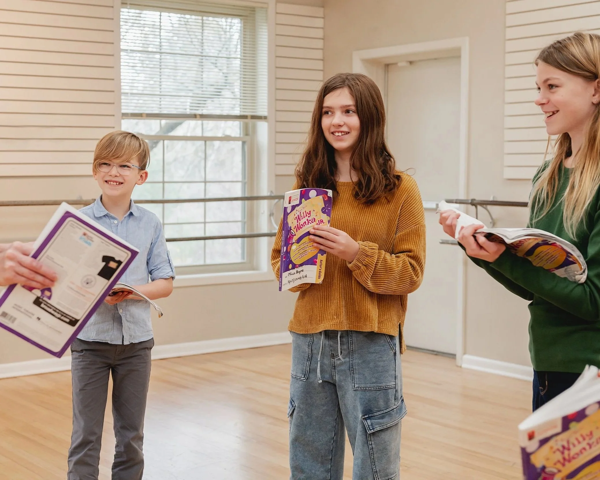 Students in rehearsal holding scripts and smiling