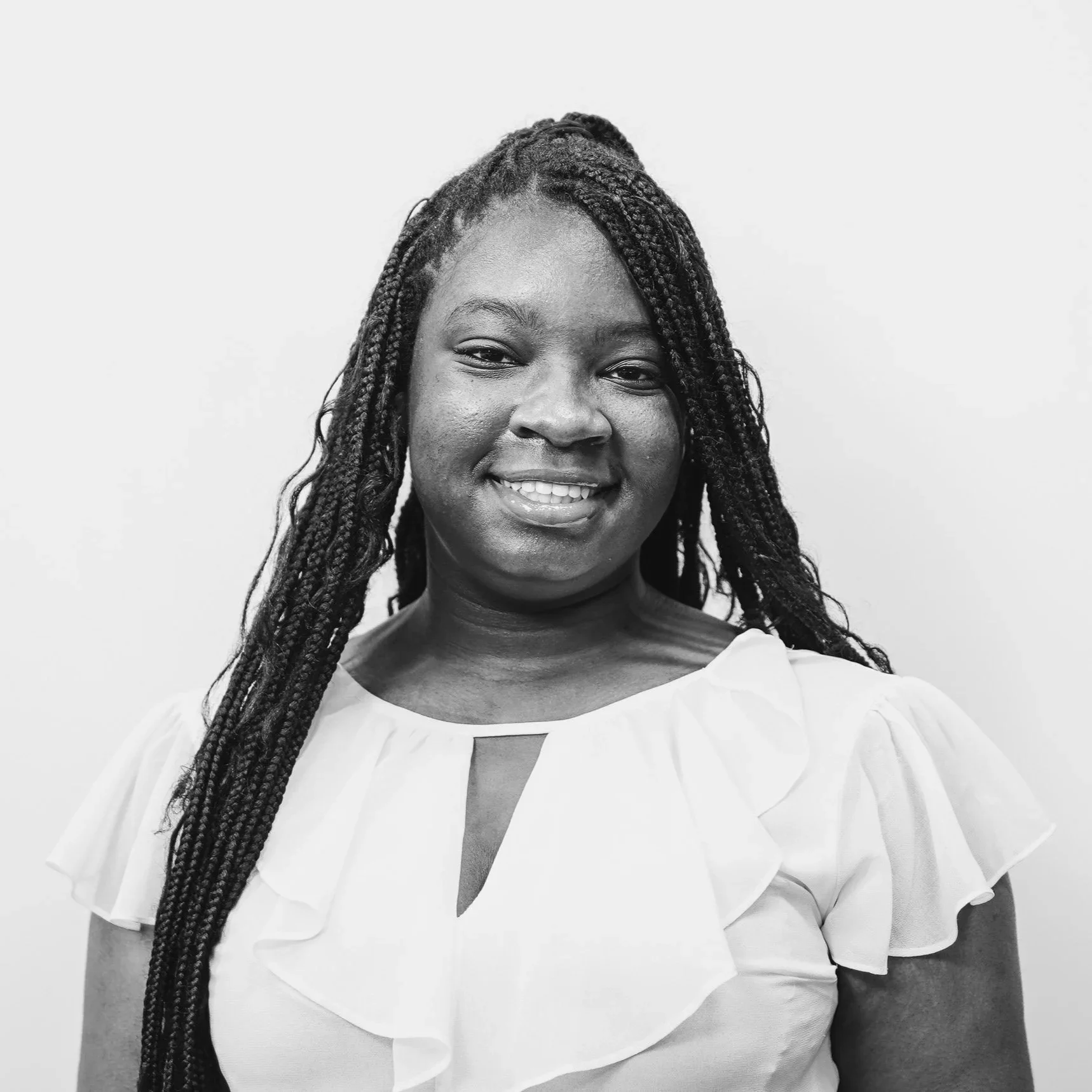 Black and white portrait of a smiling person with braided hair wearing a light-colored top.
