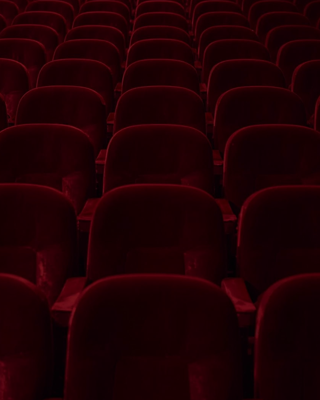 Empty red theater seats in a dark auditorium.