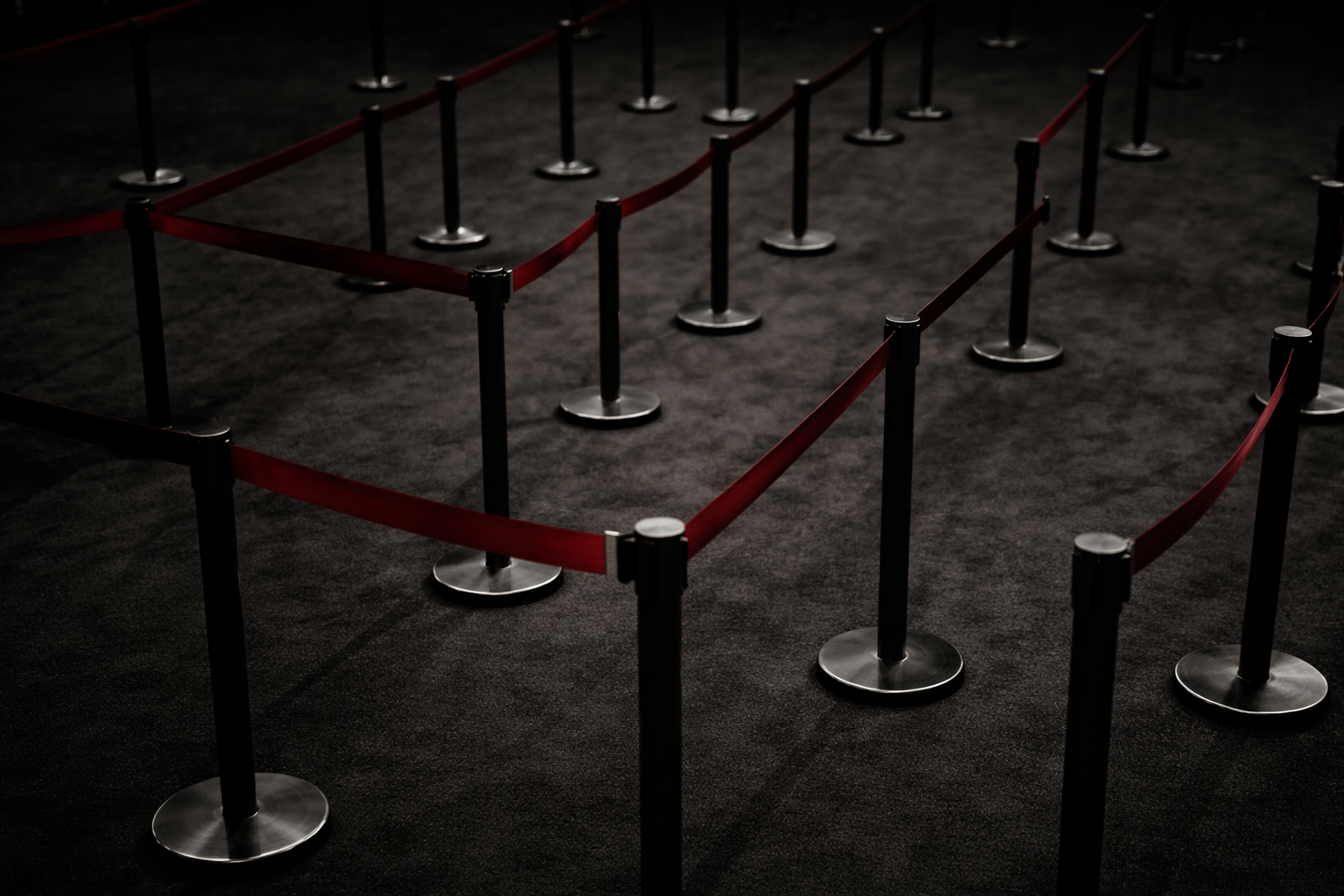 Empty red velvet rope barrier and stanchions on a dark carpeted ground, used for crowd control.