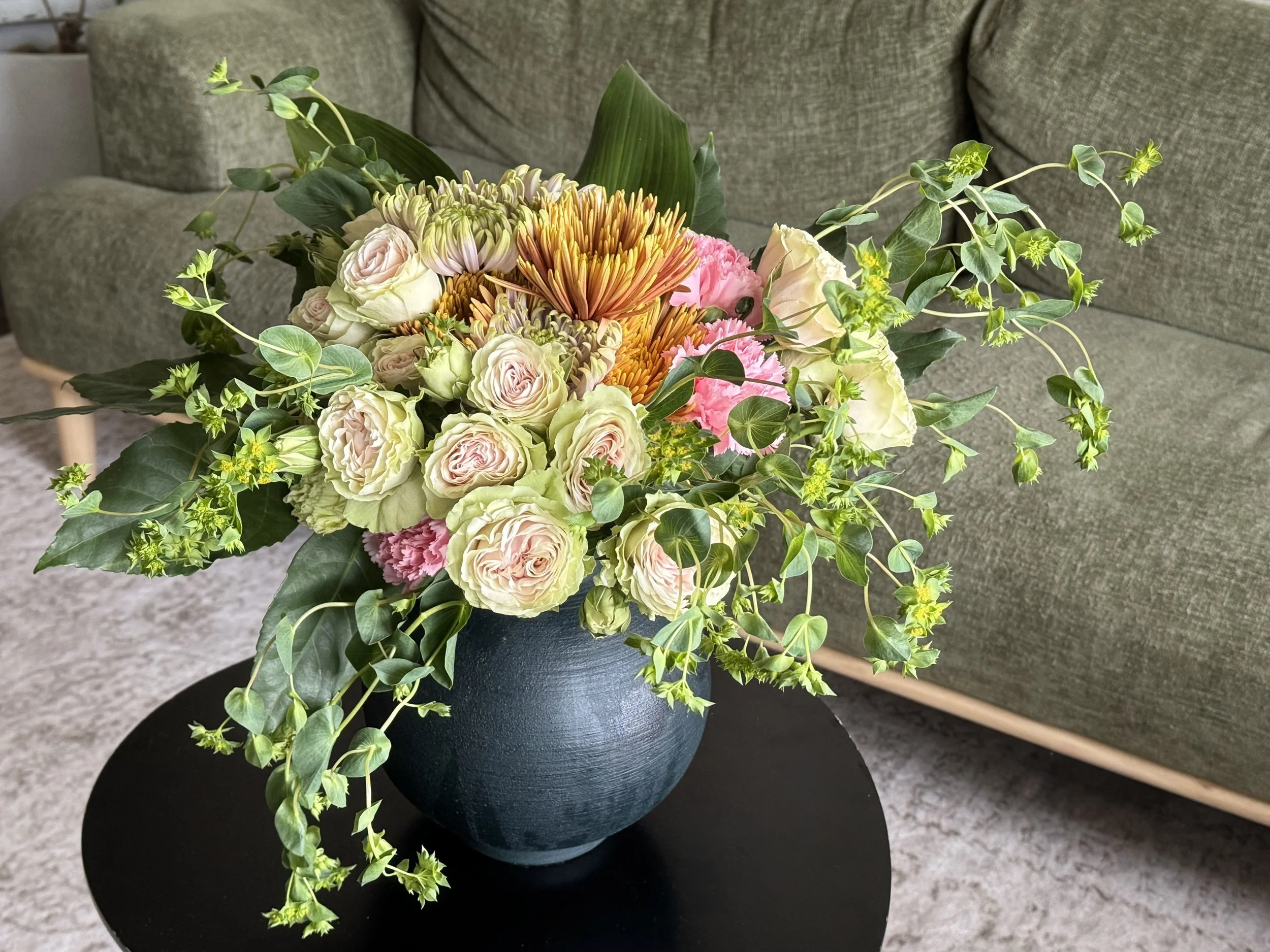 Garden roses, orange chrysanthemums and trailing greenery in a dark blue vase, a floral arrangement by Alexandra Garrett in Richmond, VA