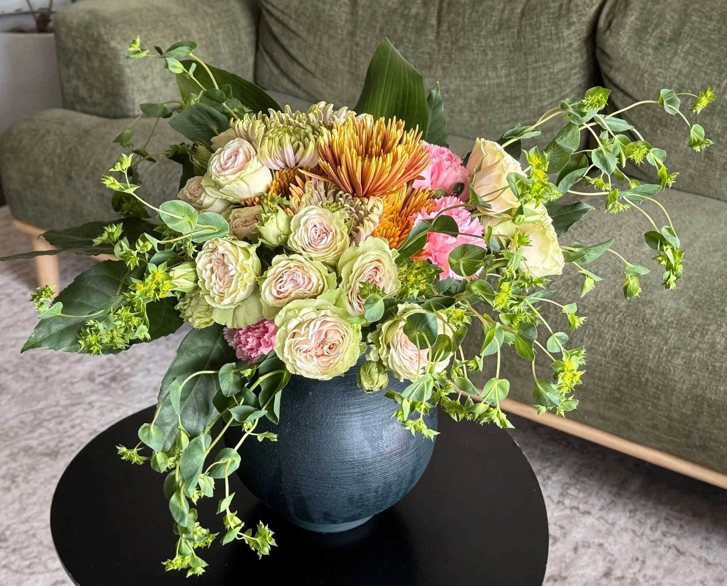 Bold floral arrangement of garden roses, orange chrysanthemums and trailing greenery in a dark blue vase by Alexandra Garrett, Richmond, VA
