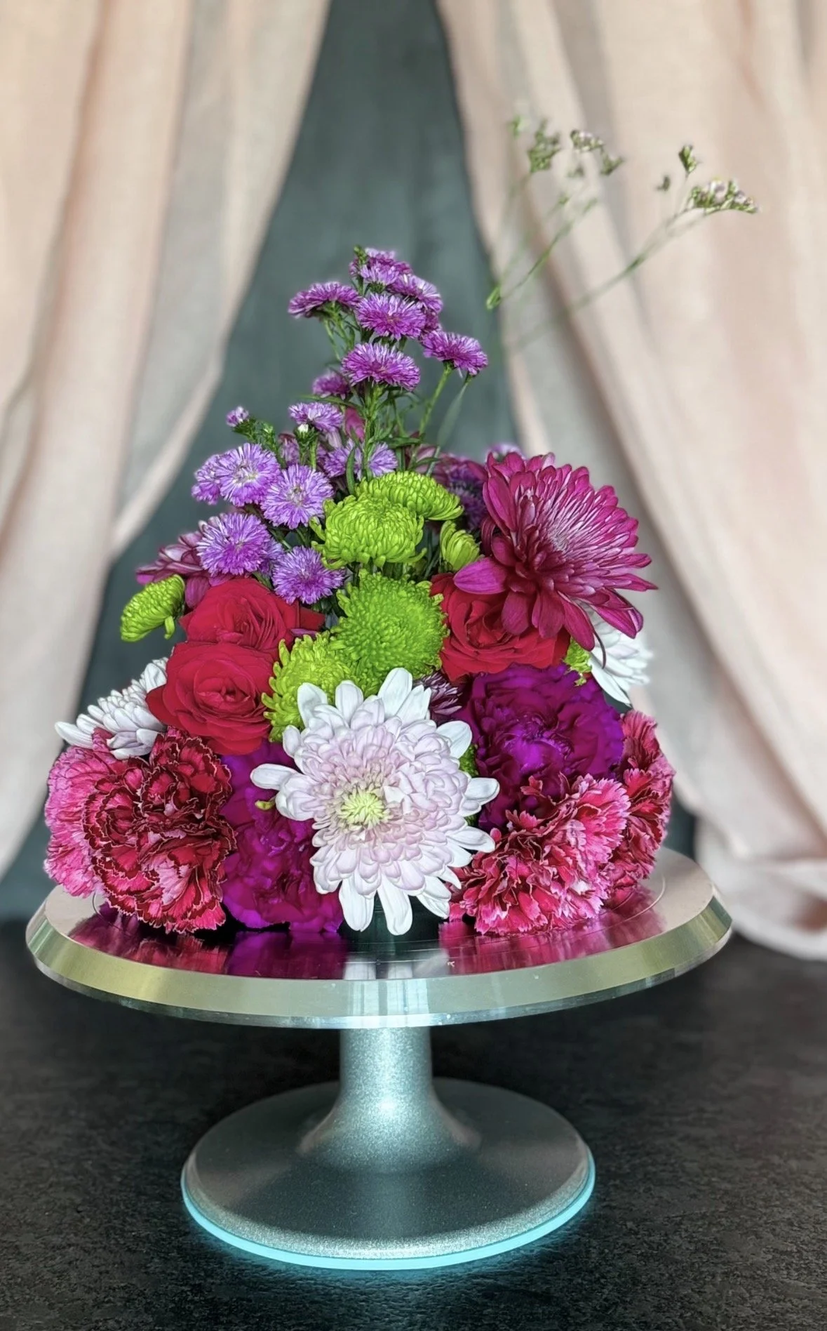 Dome of red carnations, purple and white chrysanthemums and green button mums on a glass cake stand