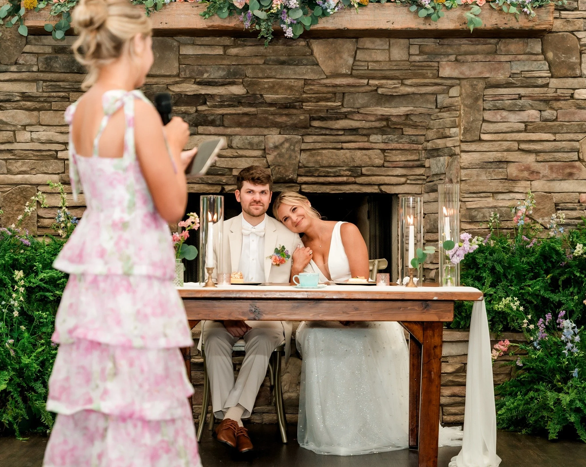 sweetheart table with hurricanes and taper candles, fireplace florals, wedding speeches