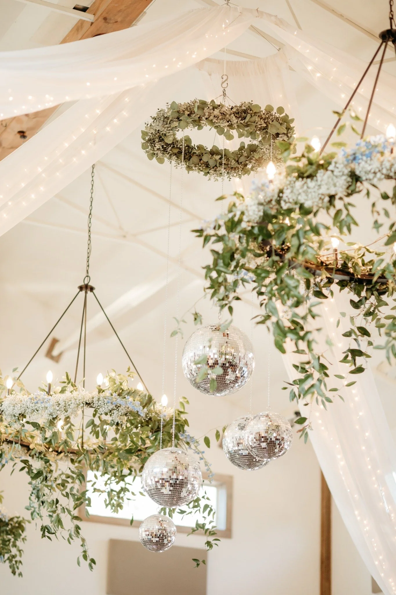 Chandeliers with greenery, Chandeliers with florals, cluster of discoballs all hanging from ceiling.