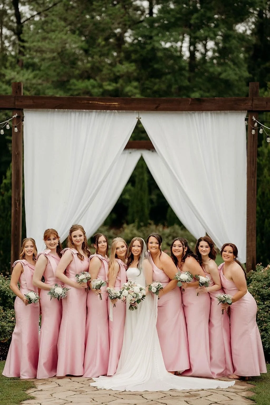 Pink bridesmaids dresses in front of outside drapery.