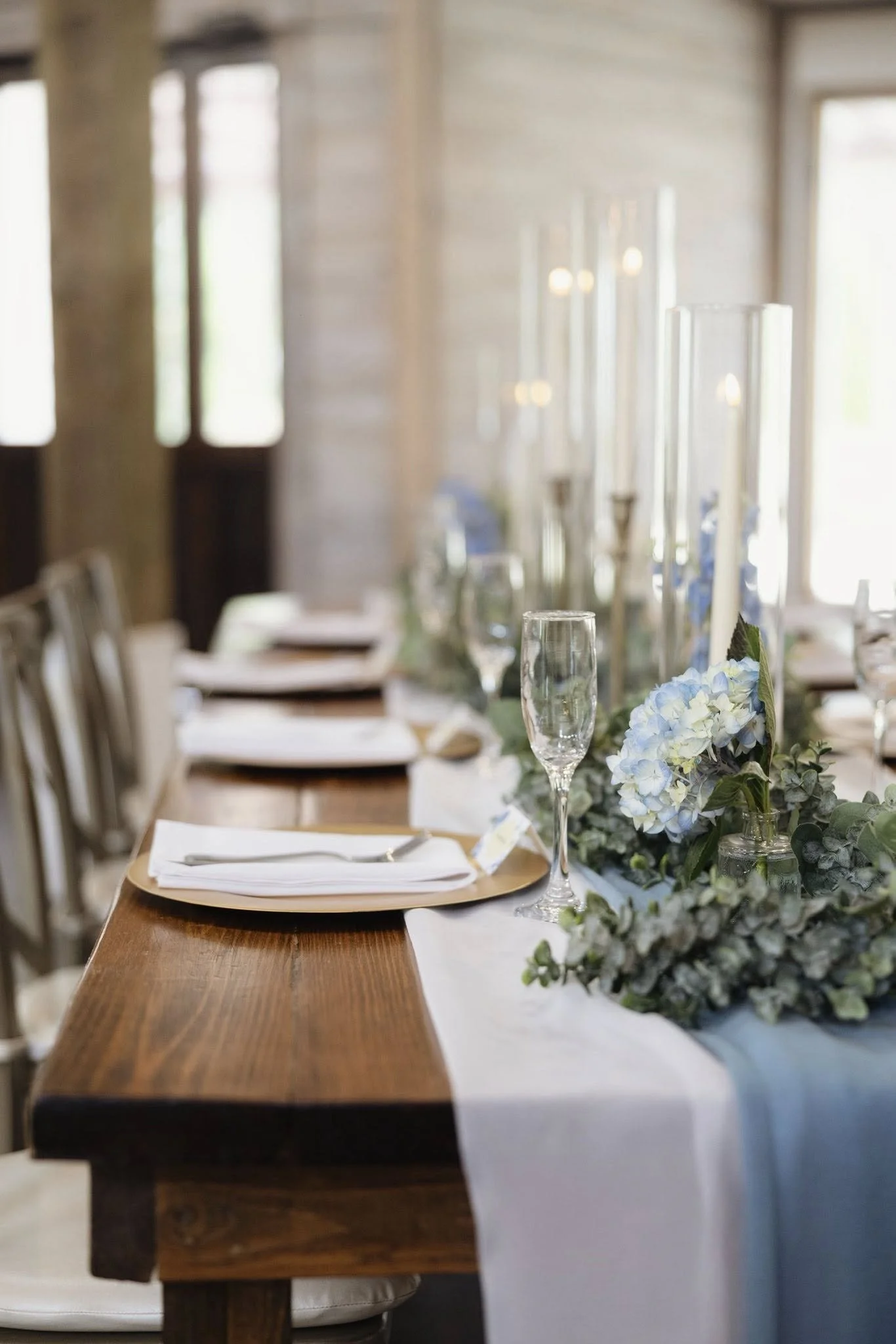 hurricanes with white taper candles, gold chargers, farmhouse table, champagne flutes wedding tablescape