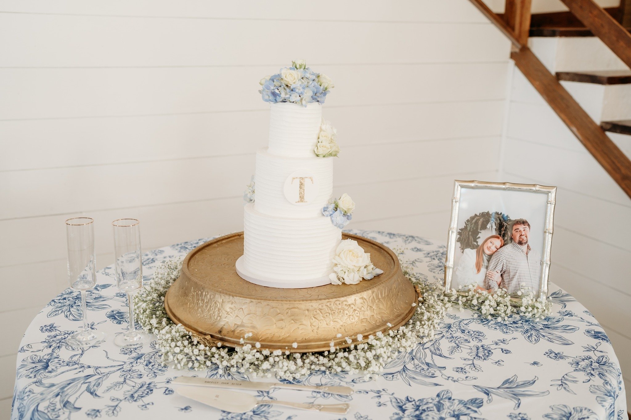 3 teir wedding cake with hydrangeas, blue floral tablecloth, gold round cake stand with baby's breath