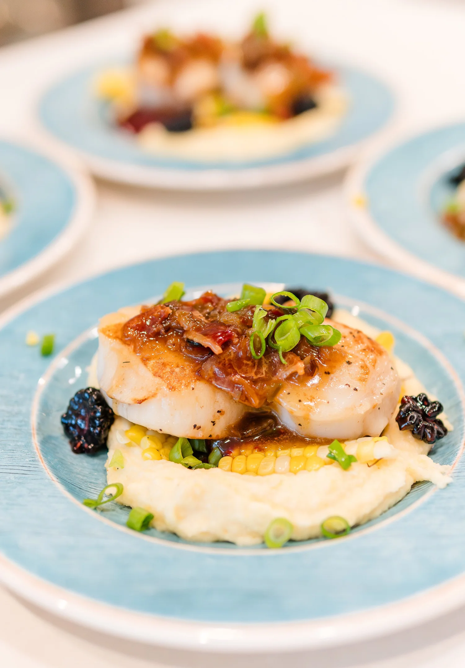 Pan-seared Gulf fish over creamy grits with corn and blackberries on a blue plate