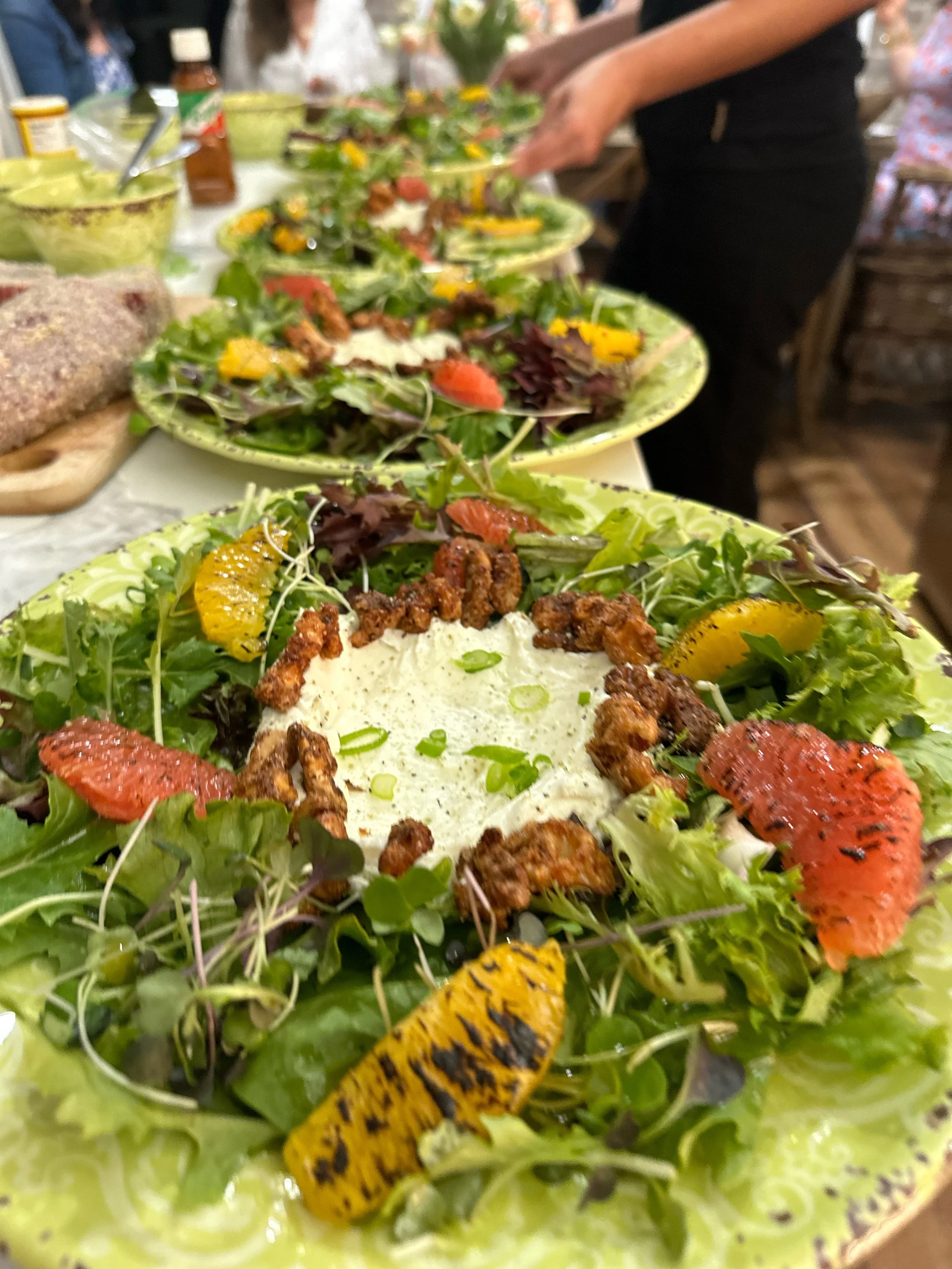 A large plate of salad with mixed greens, grilled peaches, candied pecans, and a creamy dressing, garnished with chopped green onions.