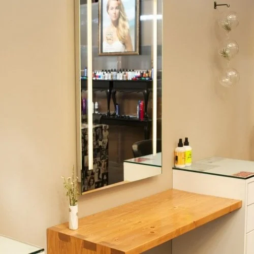 Interior of a salon with a wooden countertop, a mirror, bottles of hair products.