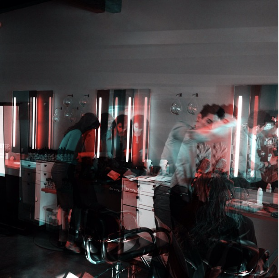 People at a salon getting haircuts, with mirrors and salon equipment, illuminated by vertical neon lights, creating a layered, ghostly effect.