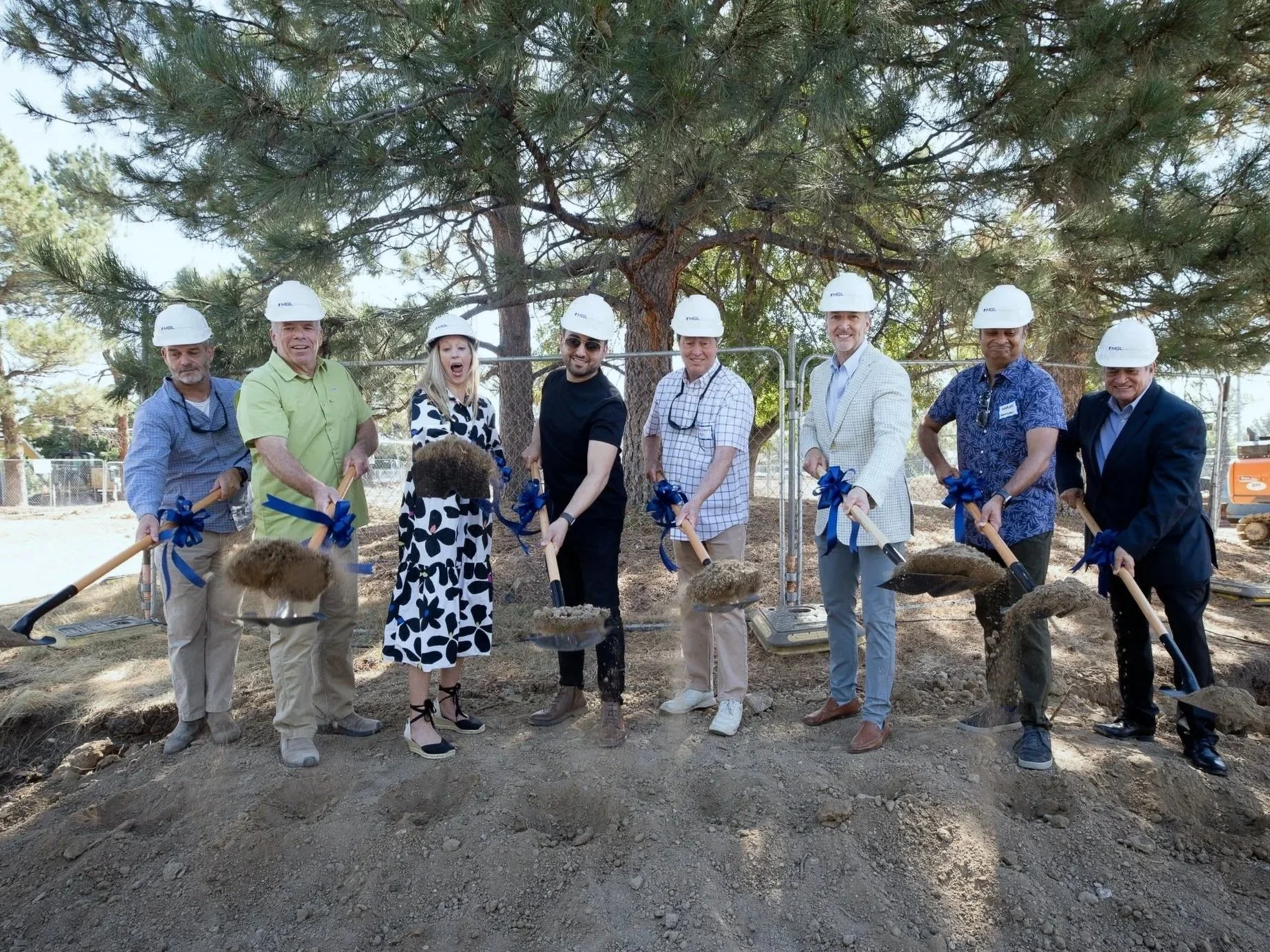 Group of corporate people wearing hard hats and holding shovels at a groundbreaking ceremony, planting a tree in a park or construction site.