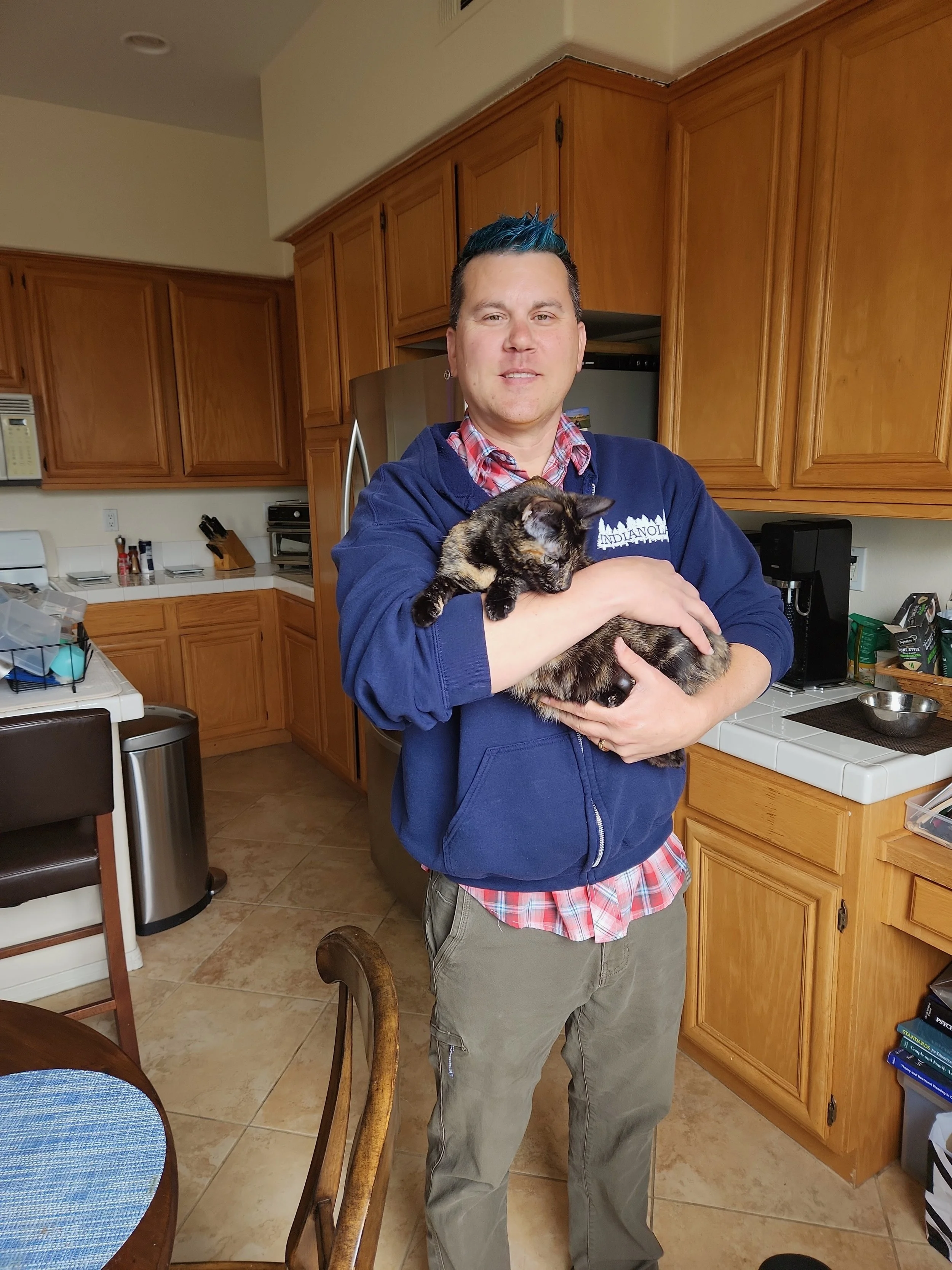 Fuzzy Buddies Pet Sitter owner, Steven, holding grey cat in a kitchen