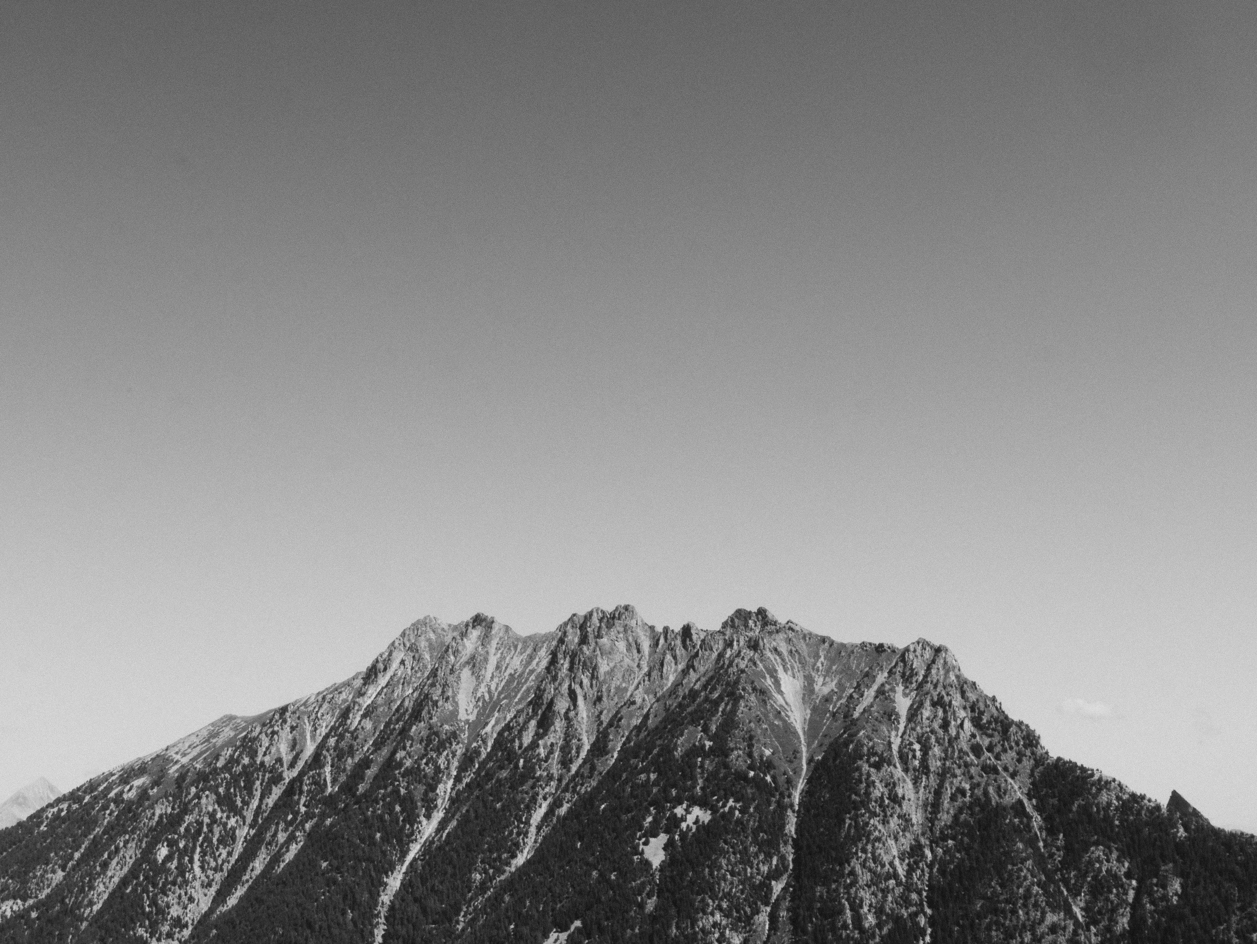 Schwarz-weiß-Berglandschaft mit hohen, felsigen Gipfeln und bewaldeten Hängen unter klaren Himmel.
